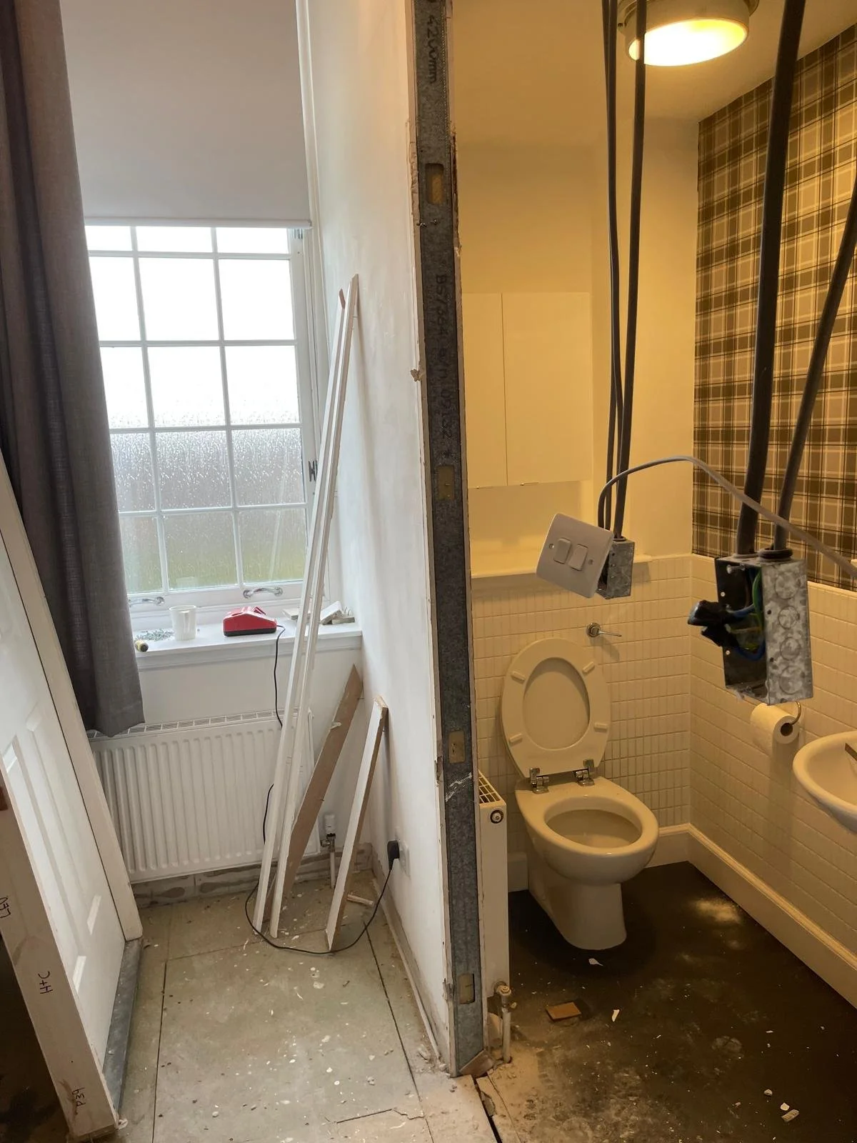 Bathroom under renovation, with construction materials and tools, and a toilet visible behind a partially assembled wall.