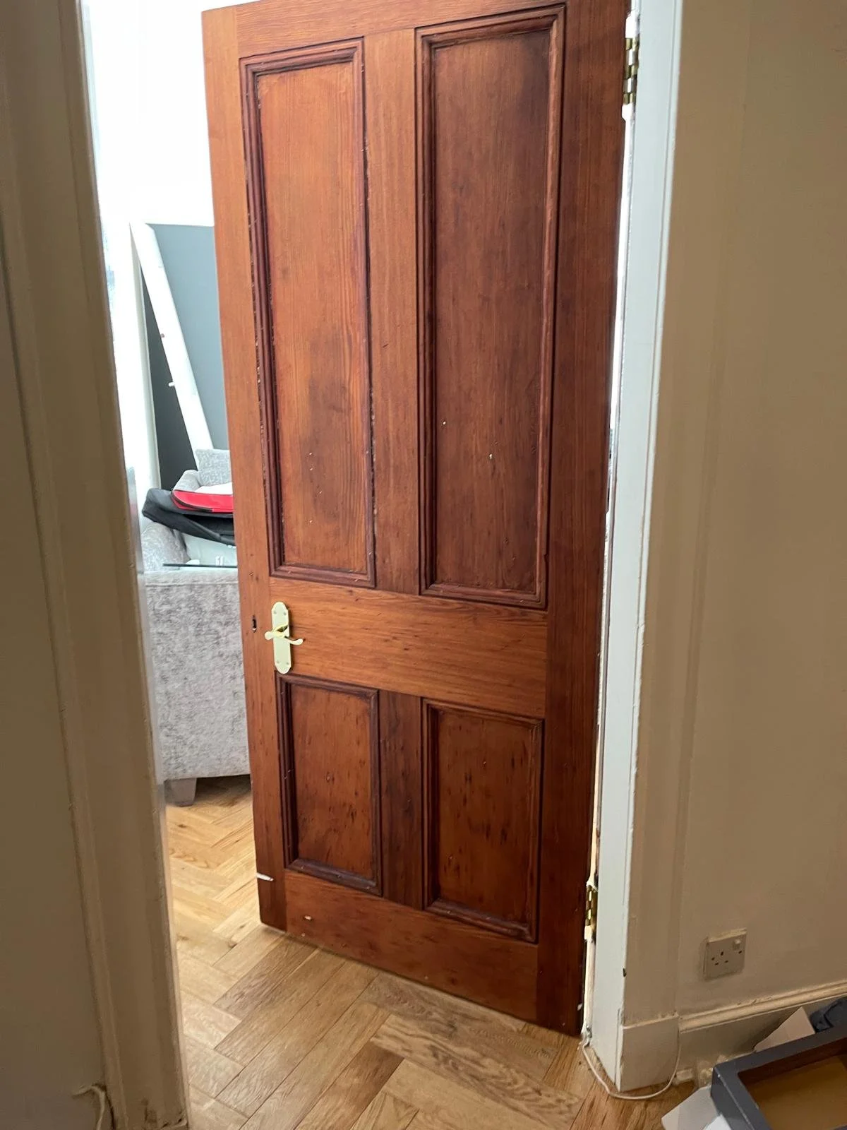 A wooden door with a brass handle, slightly open, revealing part of a living room with a gray sofa and black backpack inside.