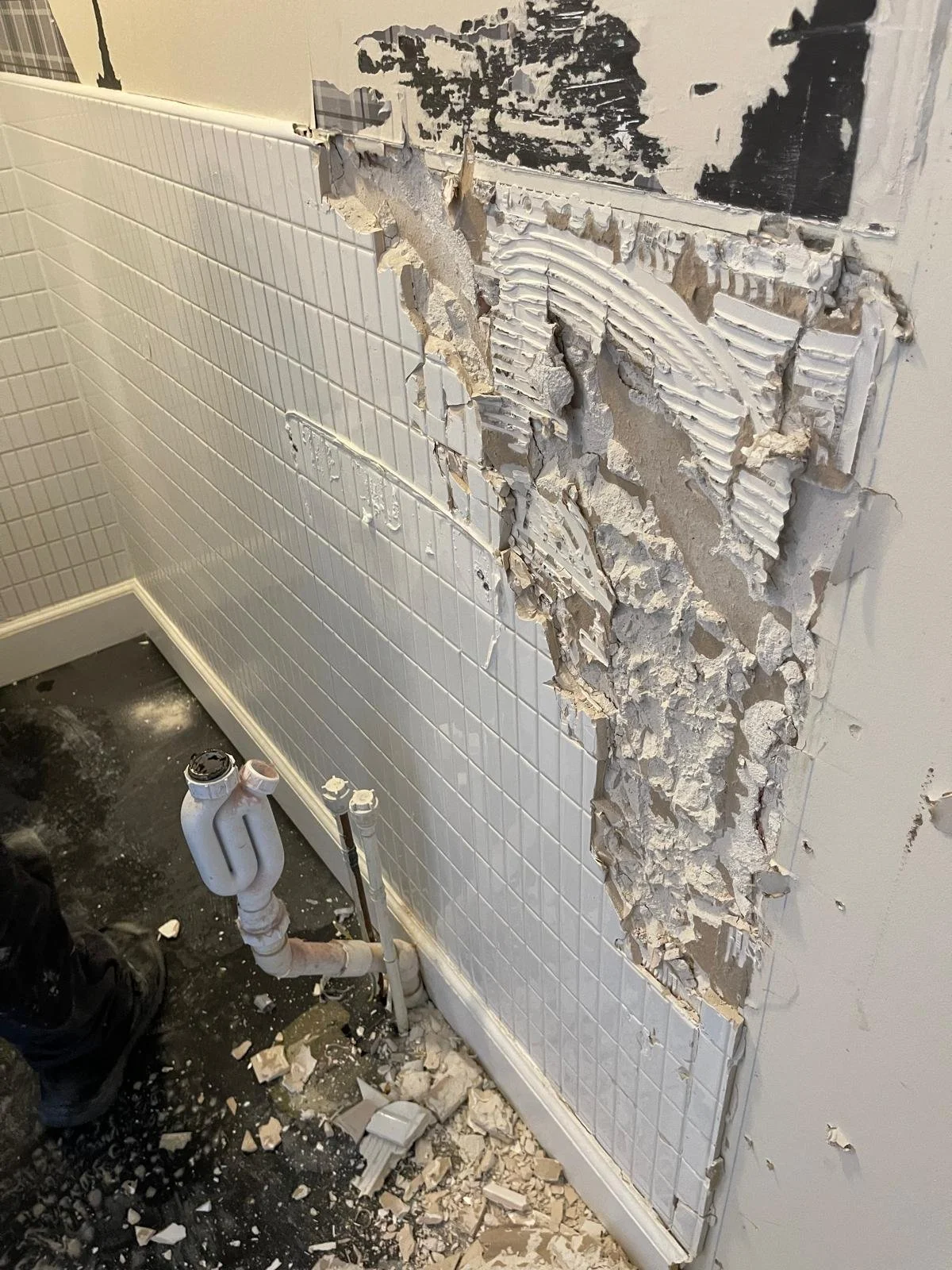 Partially demolished bathroom wall with broken tiles and exposed plumbing pipes