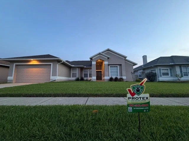 Front yard of a house with a lawn sign for pest control and a clear blue sky.