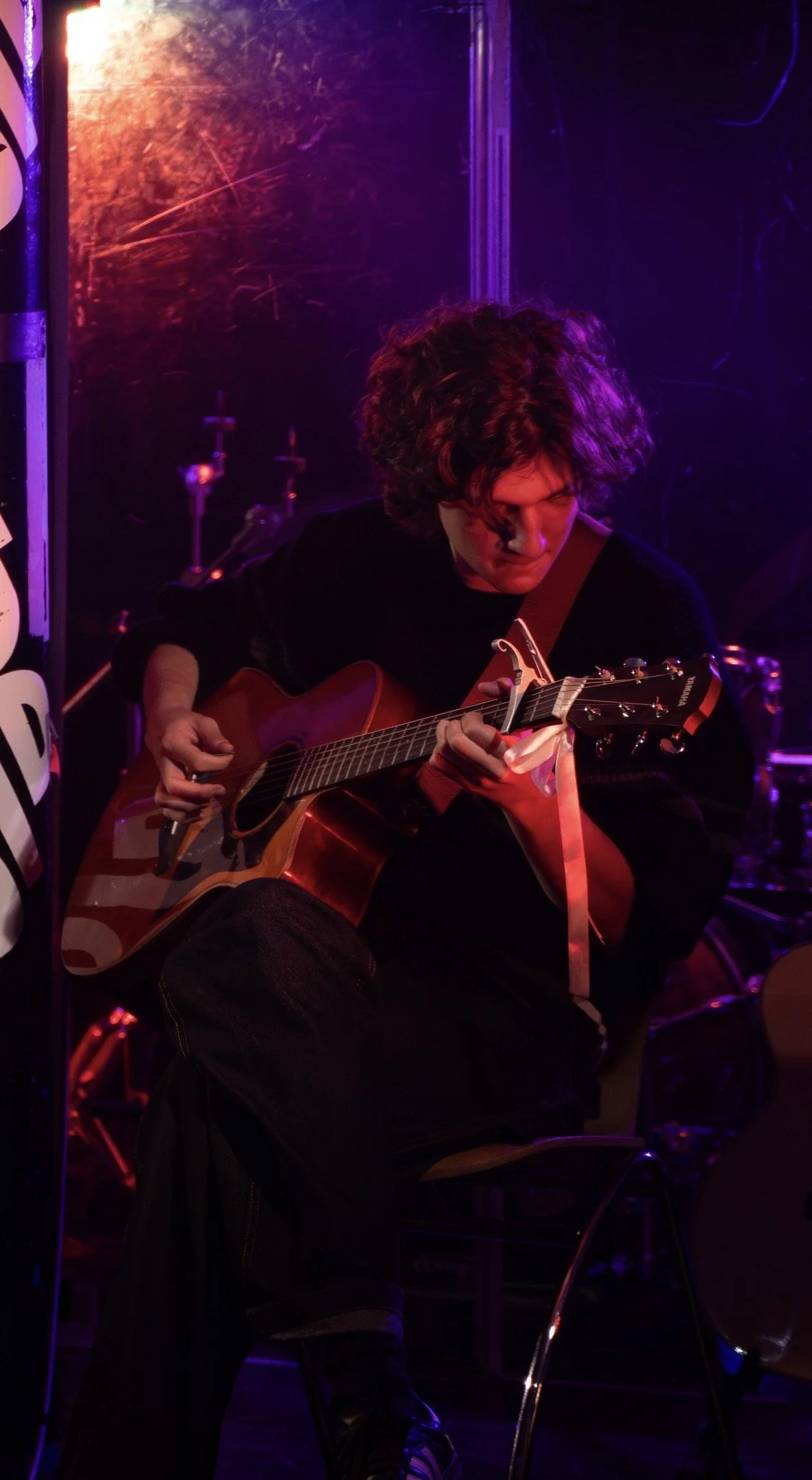 Jackson Mann playing an acoustic guitar on stage under purple and red lighting.