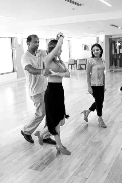 Three people practicing dance moves in a spacious studio with large windows.