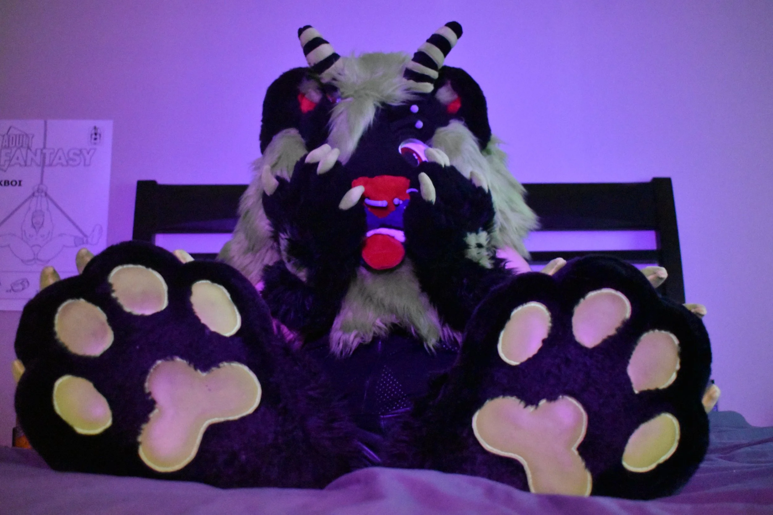 Person in a lion costume sitting on a plush bedspread featuring large paw prints, with a purple-lit background and a poster on the wall behind.