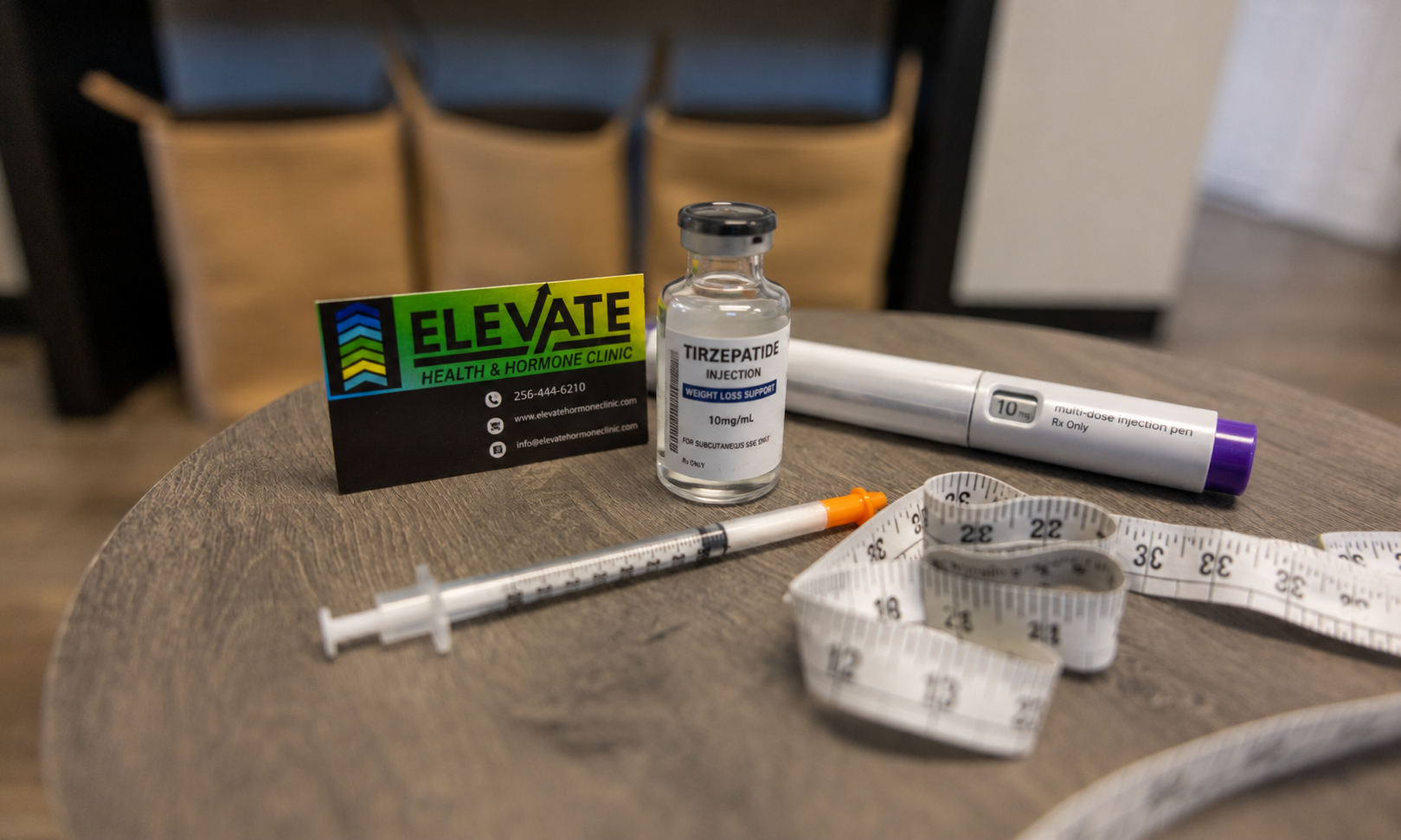 A wooden table with a business card from Elevate Health & Hormone Clinic, a bottle of Tirzepatide injection, a multi-dose injection pen, a syringe, and a measuring tape.