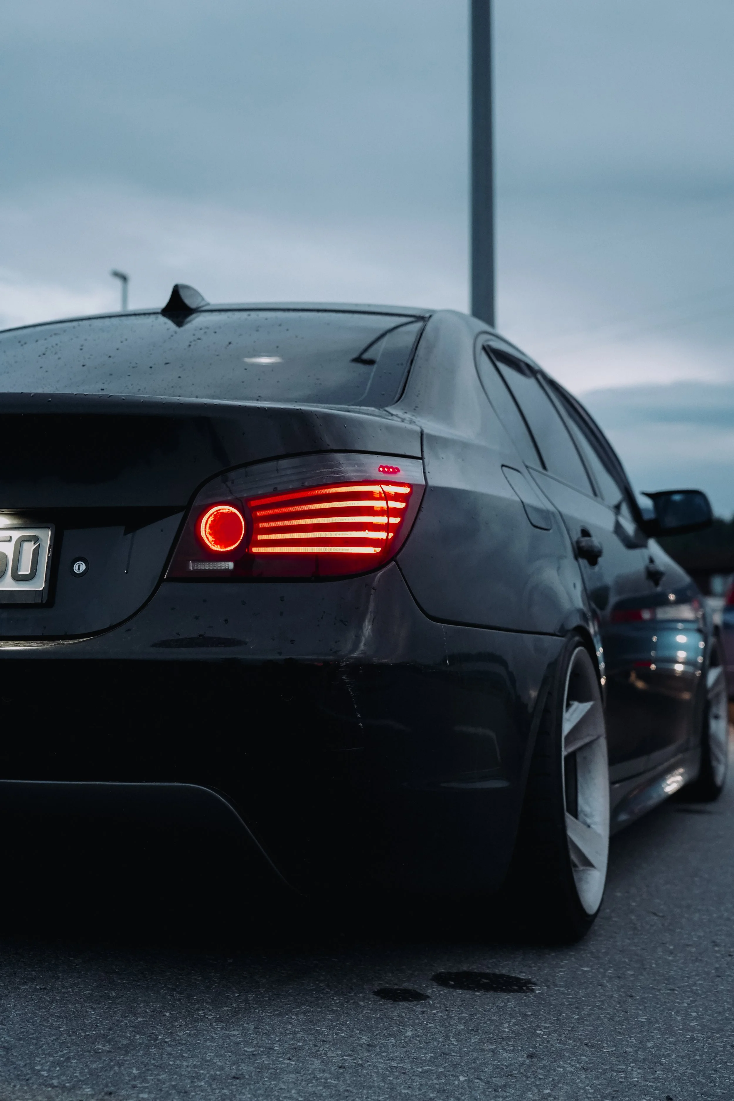 Krupni plan osvijetljenog stražnjeg LED svjetla i širokih naplataka na crnom BMW-u serije 5 E60.