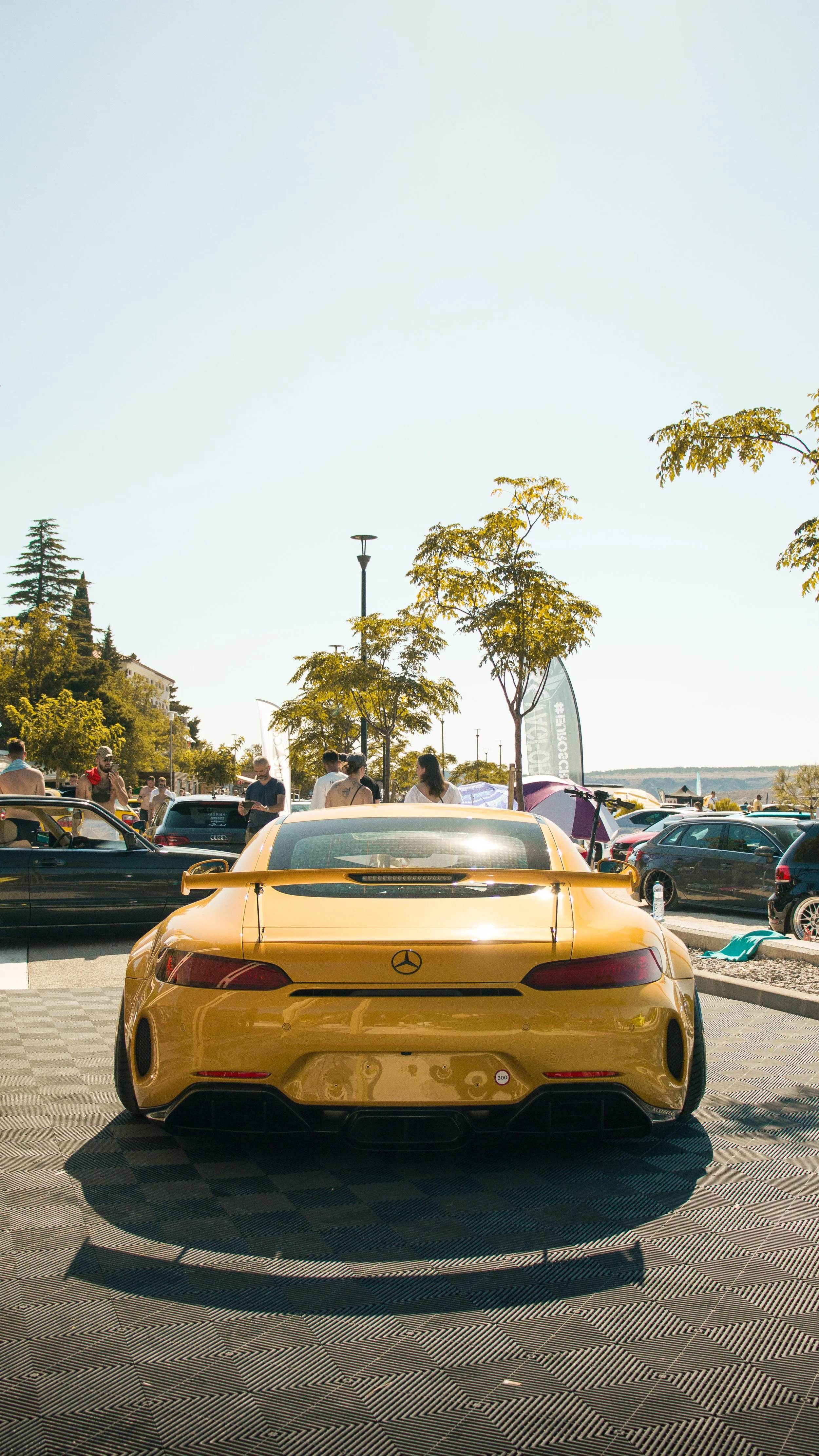Stražnji dio žutog Mercedes-AMG GT s velikim bojler spojlerom parkiran na auto skupu uz obalu.