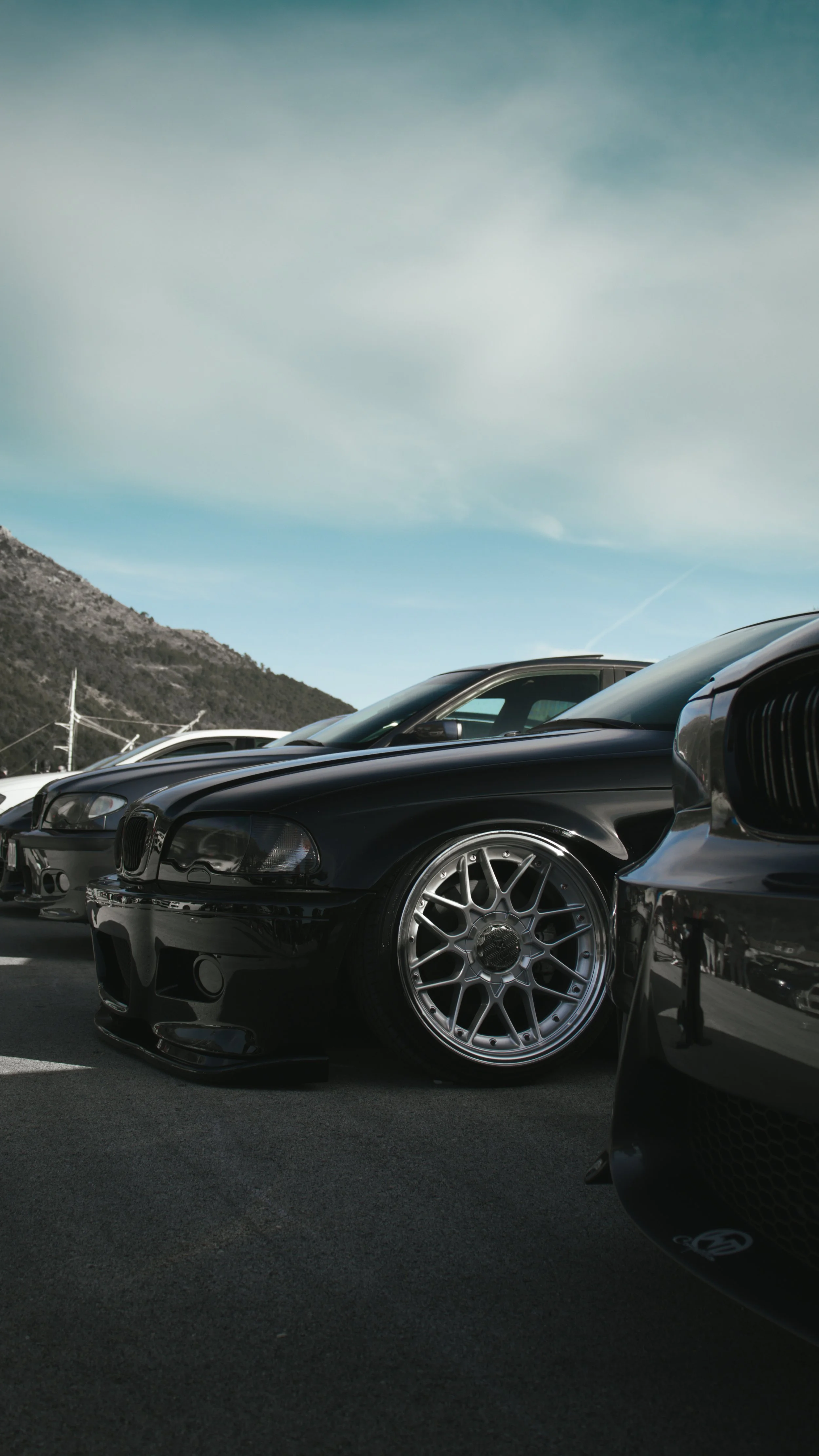 Profesionalna fotografija niskog kuta koja prikazuje spušteni crni BMW E46 s detaljima mrežastih felgi na automobilskom skupu u Hrvatskoj.