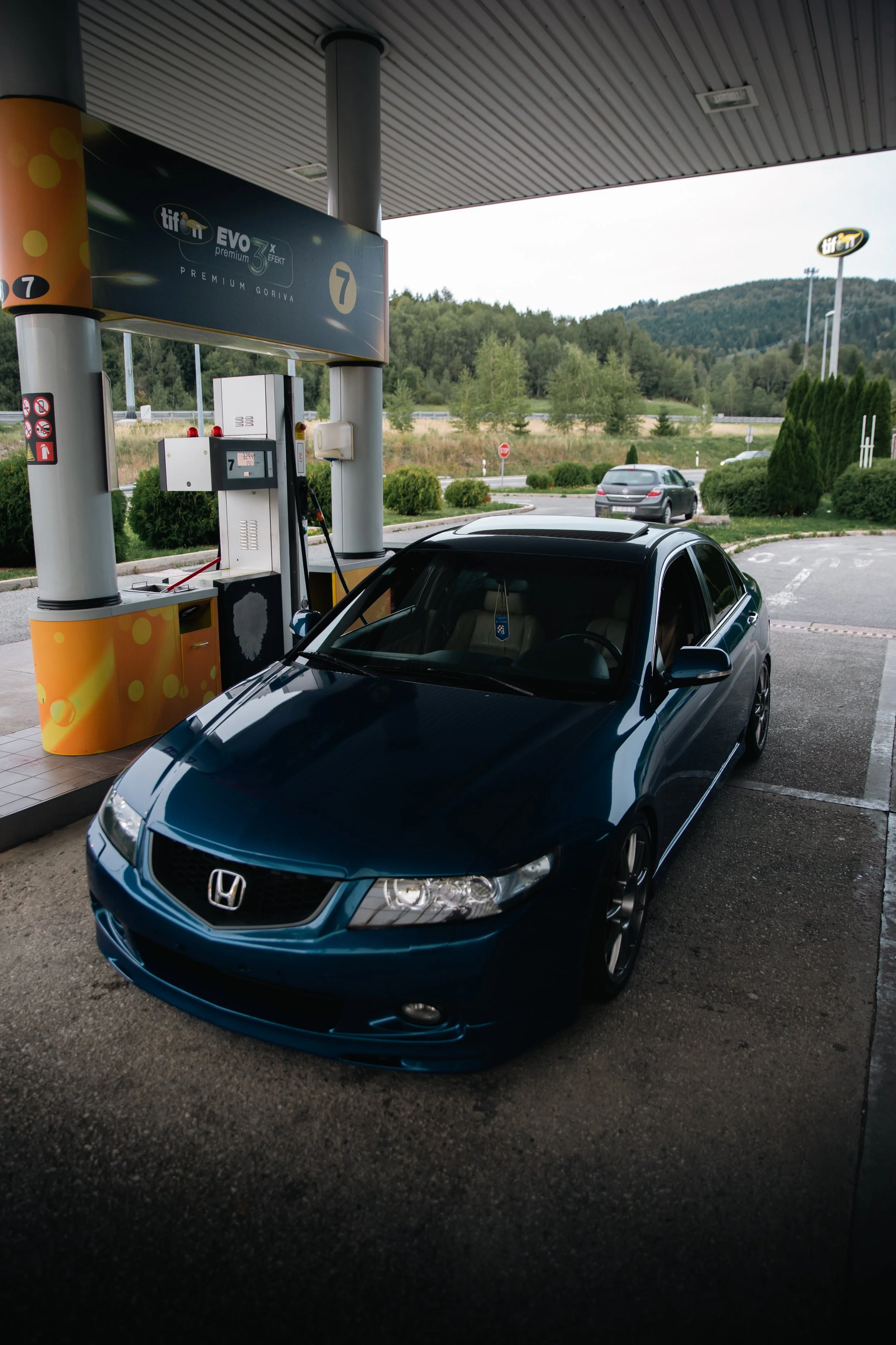 Tamnoplava spuštena Honda Accord sedme generacije parkirana na Tifon benzinskoj crpki pod noćnim osvjetljenjem.