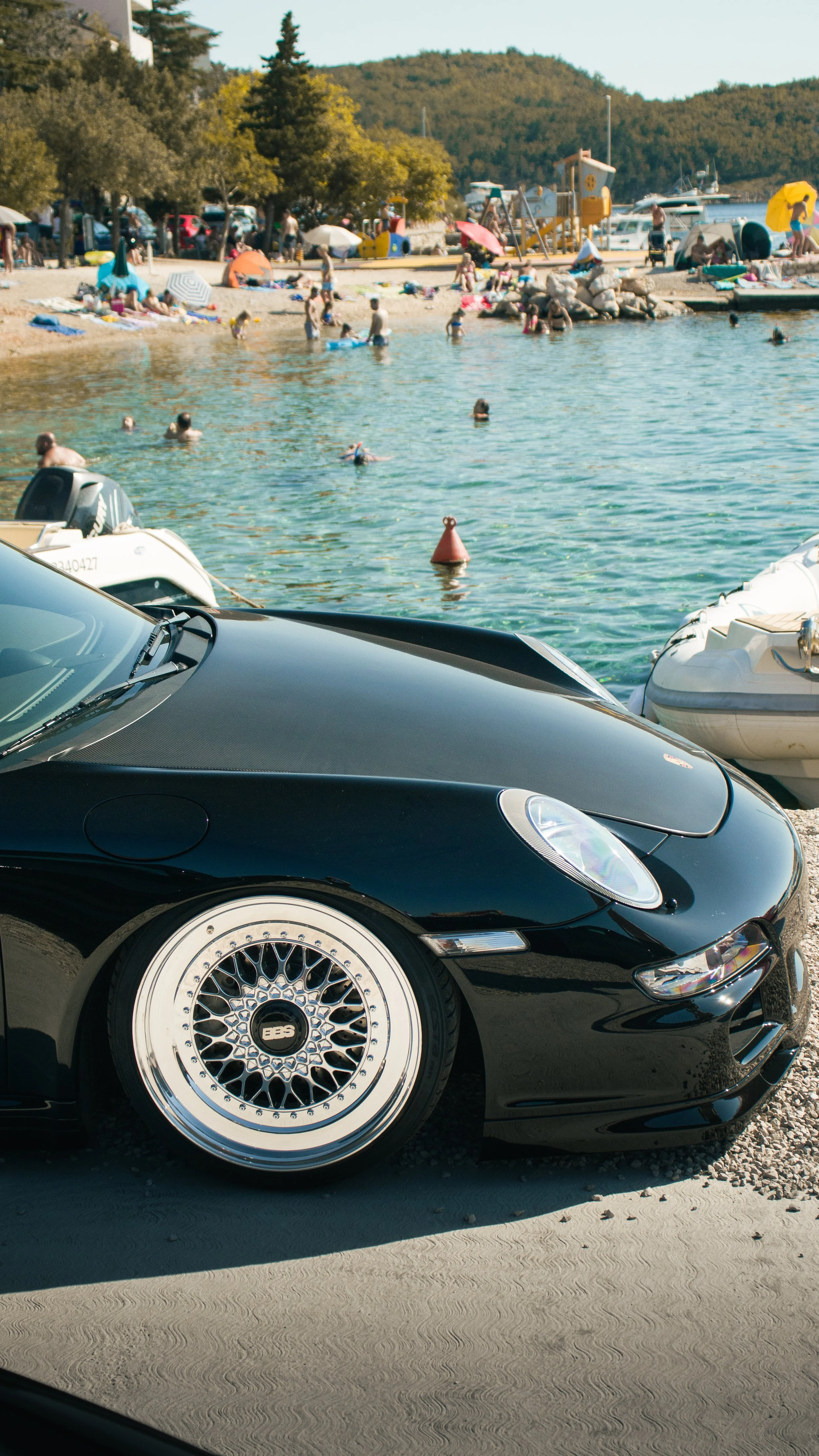 Detaljni kadar prednjeg dijela crnog Porschea 911 sa sjajnim BBS višekrakim naplatcima uz morsku obalu.