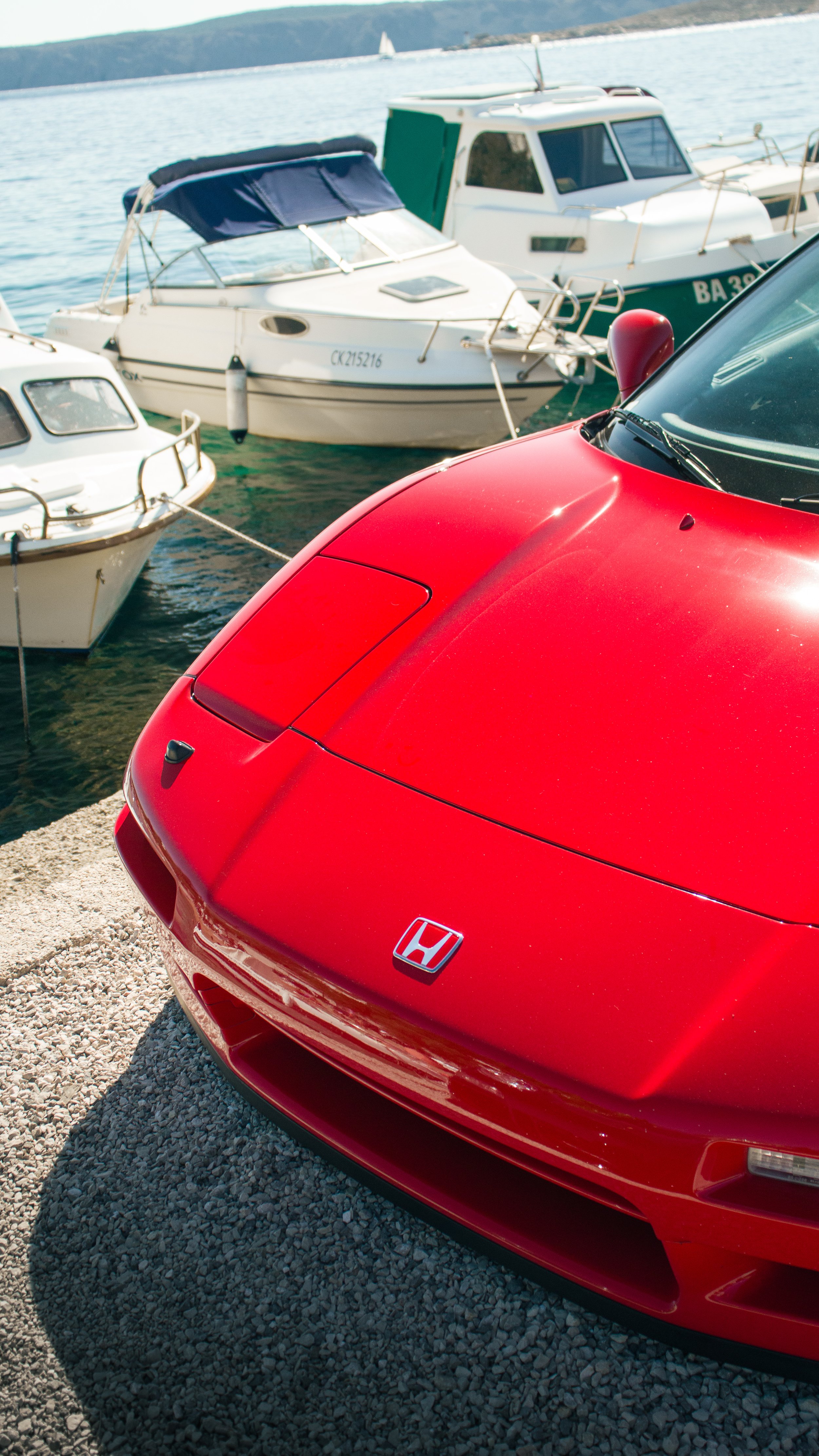 Detalj prednjeg poklopca i pop-up svjetala crvene Honde NSX parkirane uz brodove na obali.