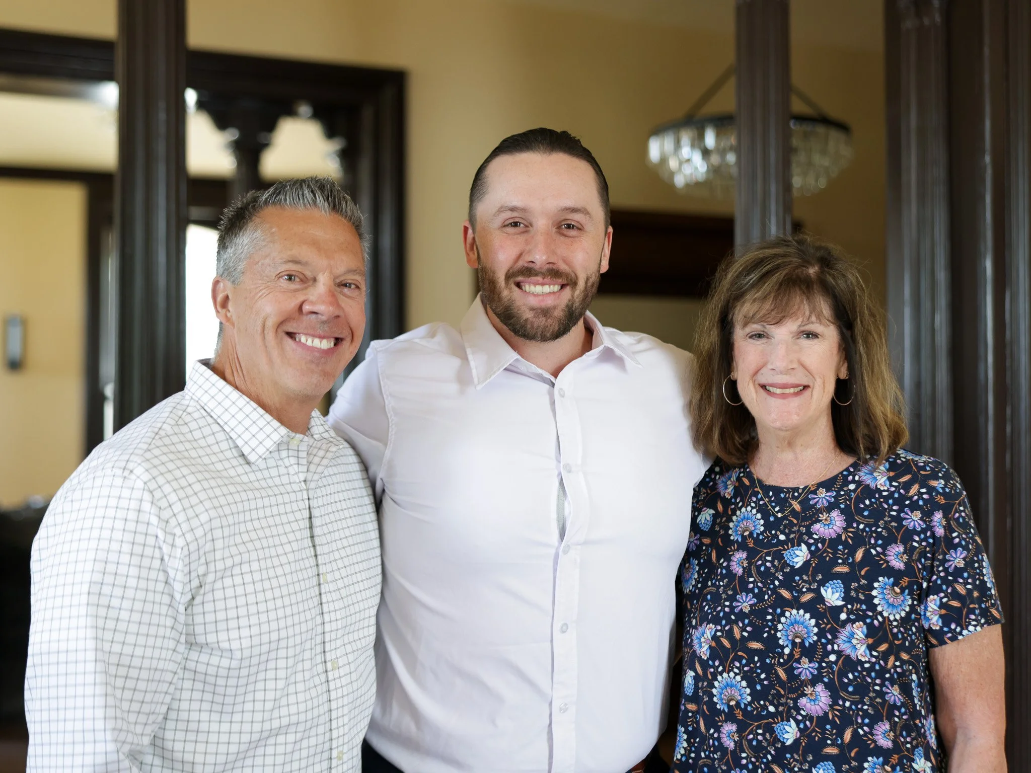 Table 1888 owners smiling in a room with chandelier, three men and one woman, close-up portrait