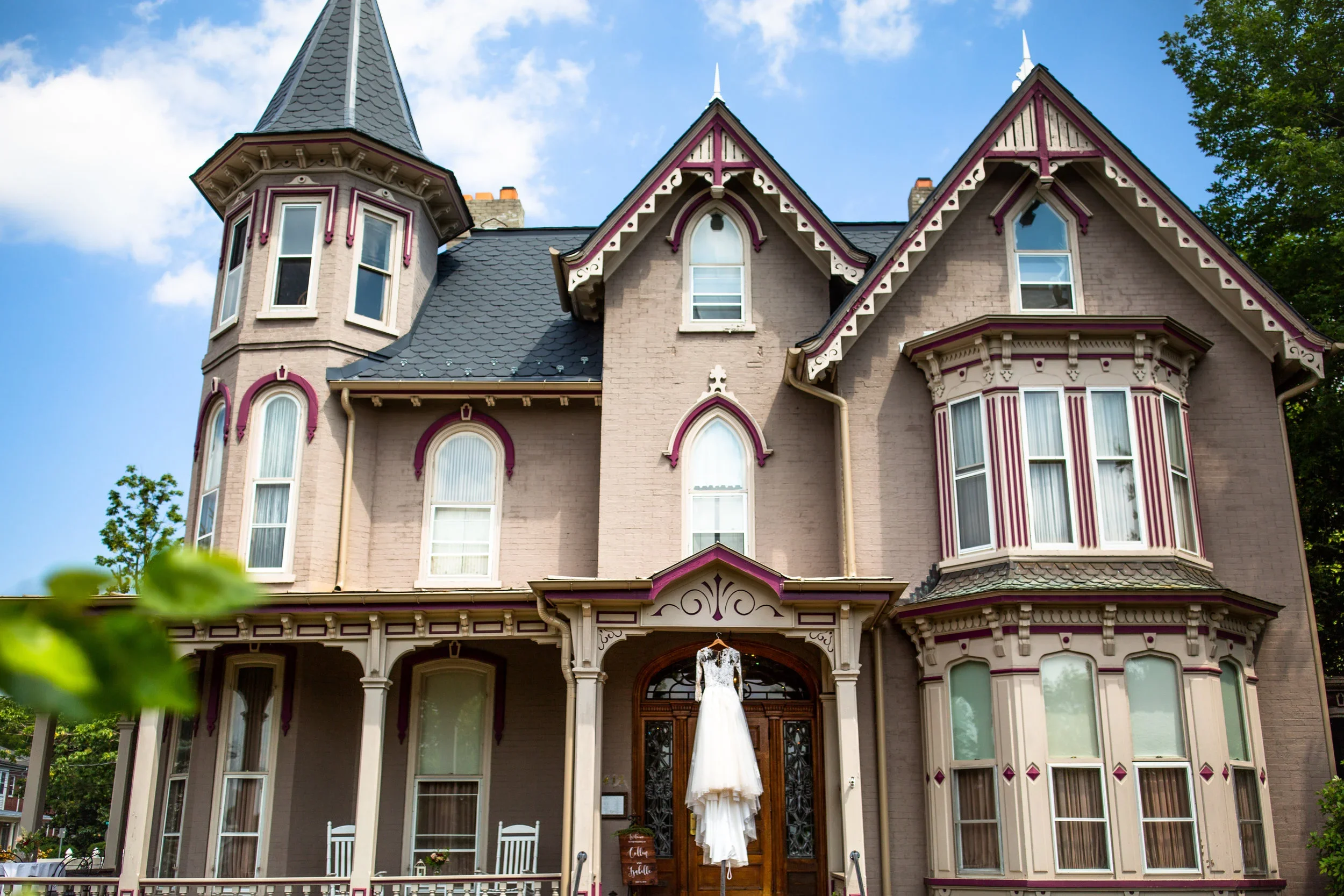 The exterior of Table 1888: A large Victorian-style house with a tower, decorated trim, and multiple windows, set against a blue sky with some clouds.