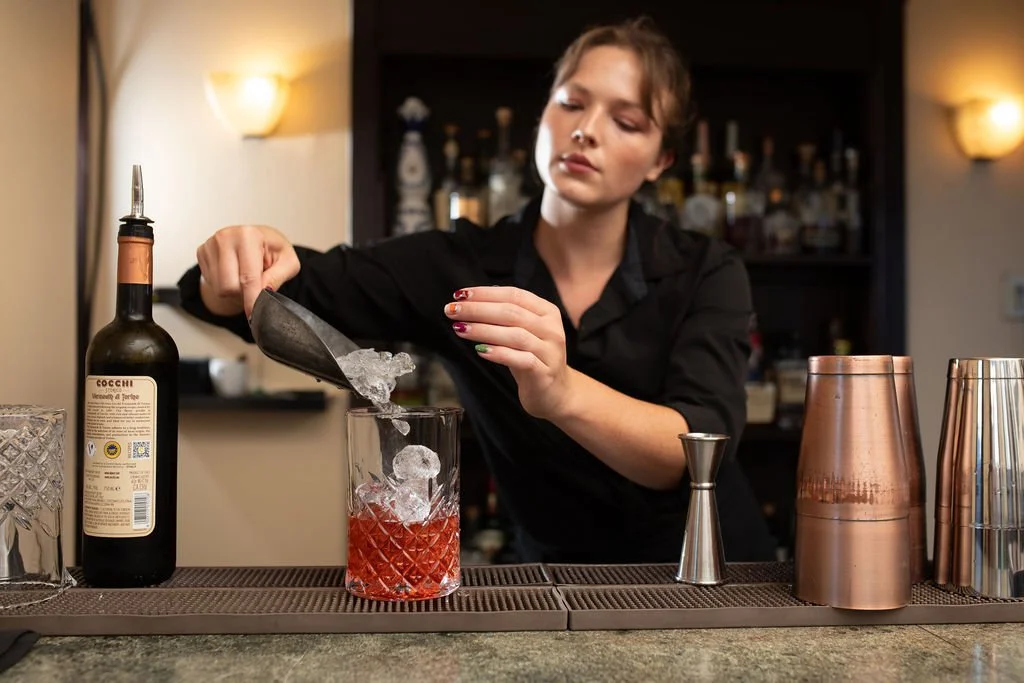 A bartender preparing a cocktail with ice in a glass at a bar counter.