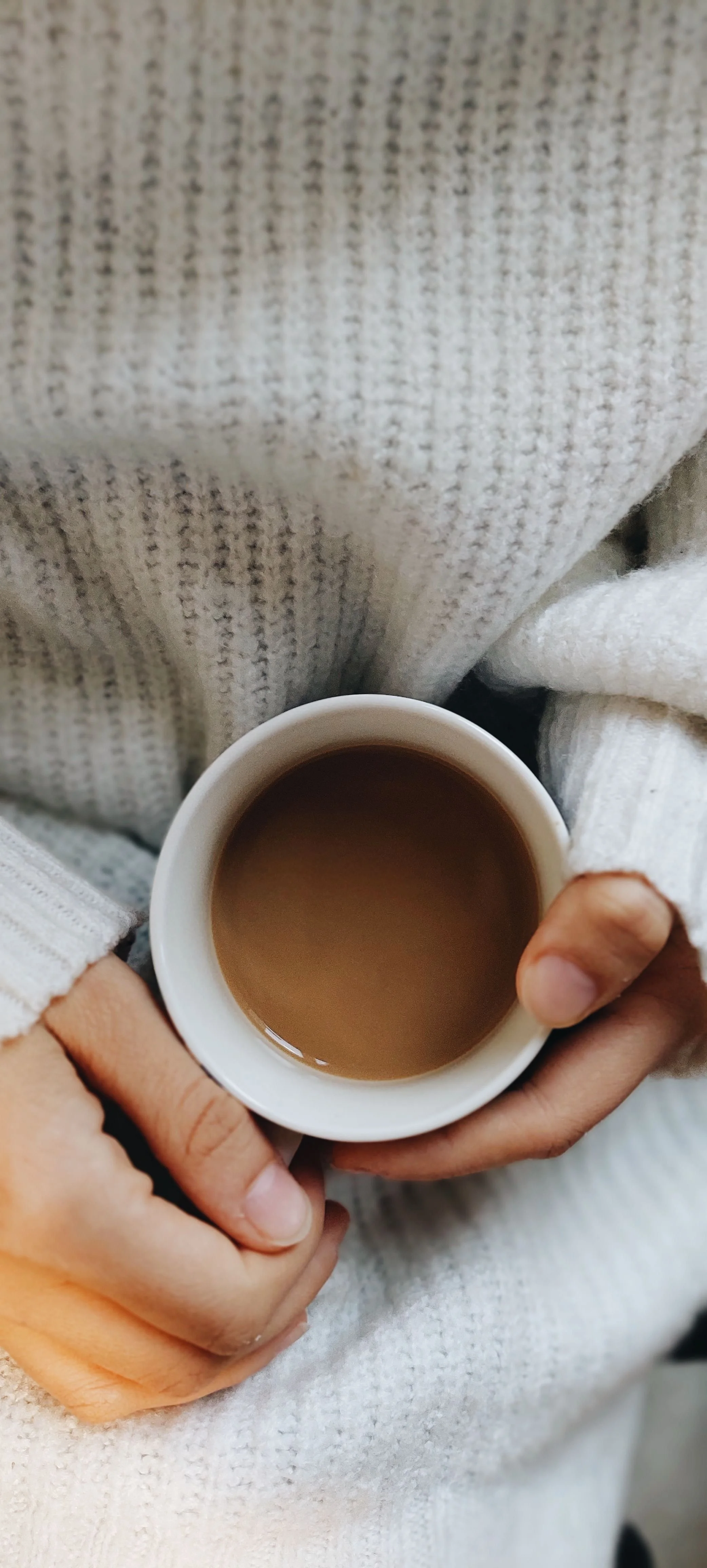 Person holding a white mug filled with coffee, wearing a cozy white sweater.