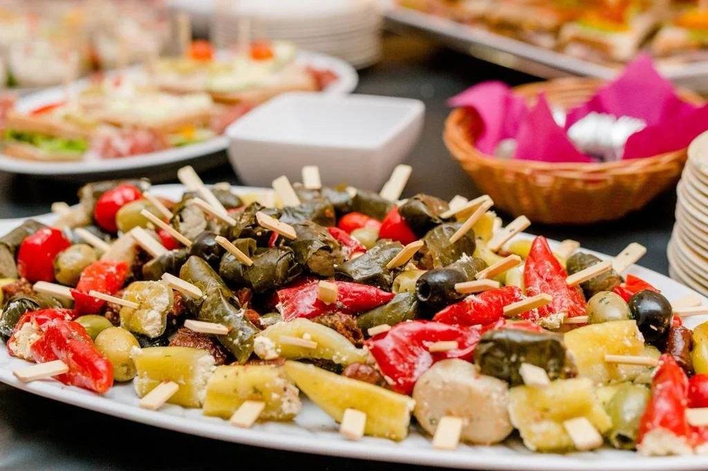 Verschiedene Antipasti auf einem Teller, darunter eingelegte Paprika, Oliven, Artischocken und Käse, serviert auf einem Buffet.