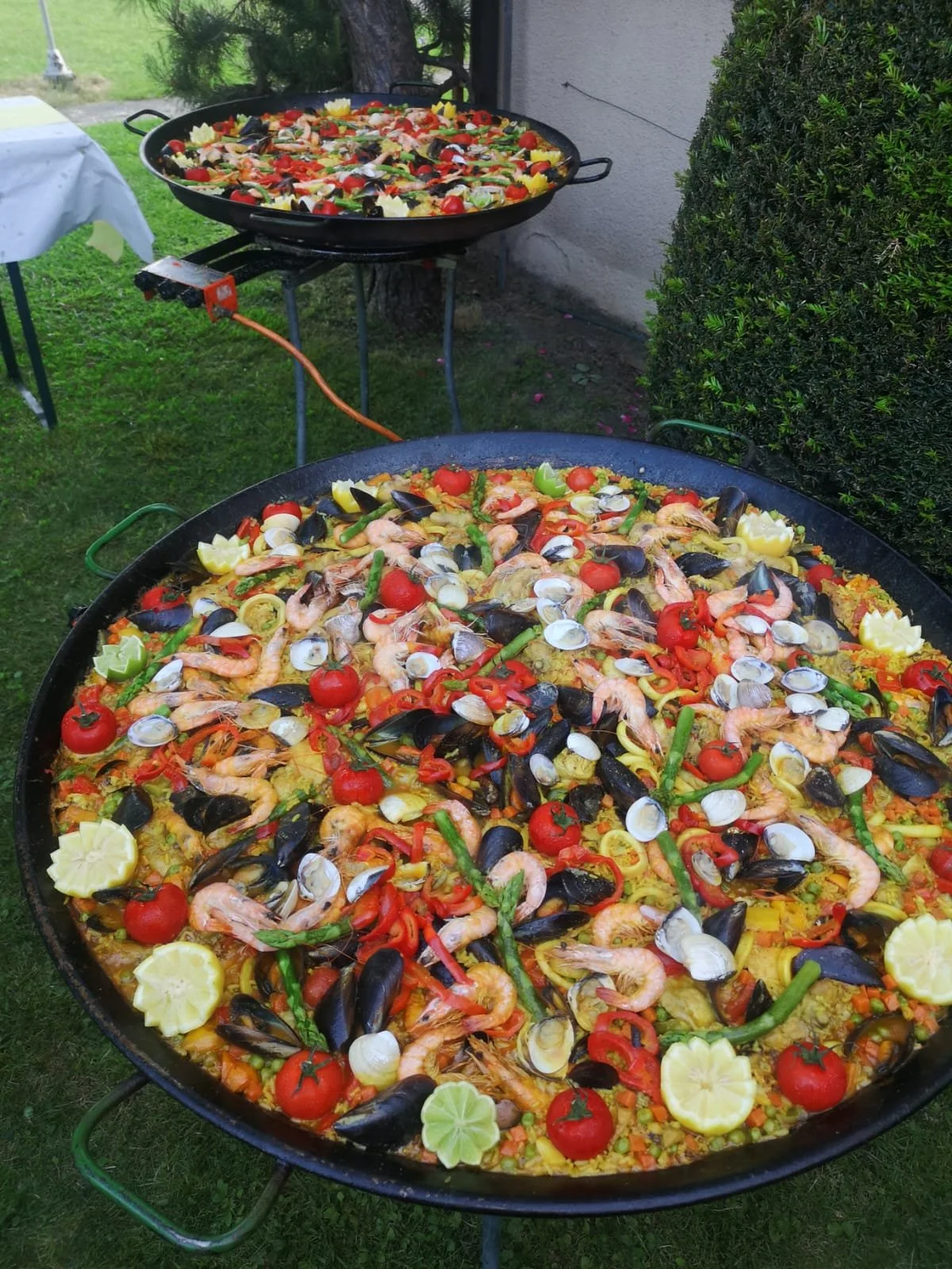 Große Paella mit Meeresfrüchten, Tomaten, Paprika, Zitronen und grünen Bohnen im Freien.