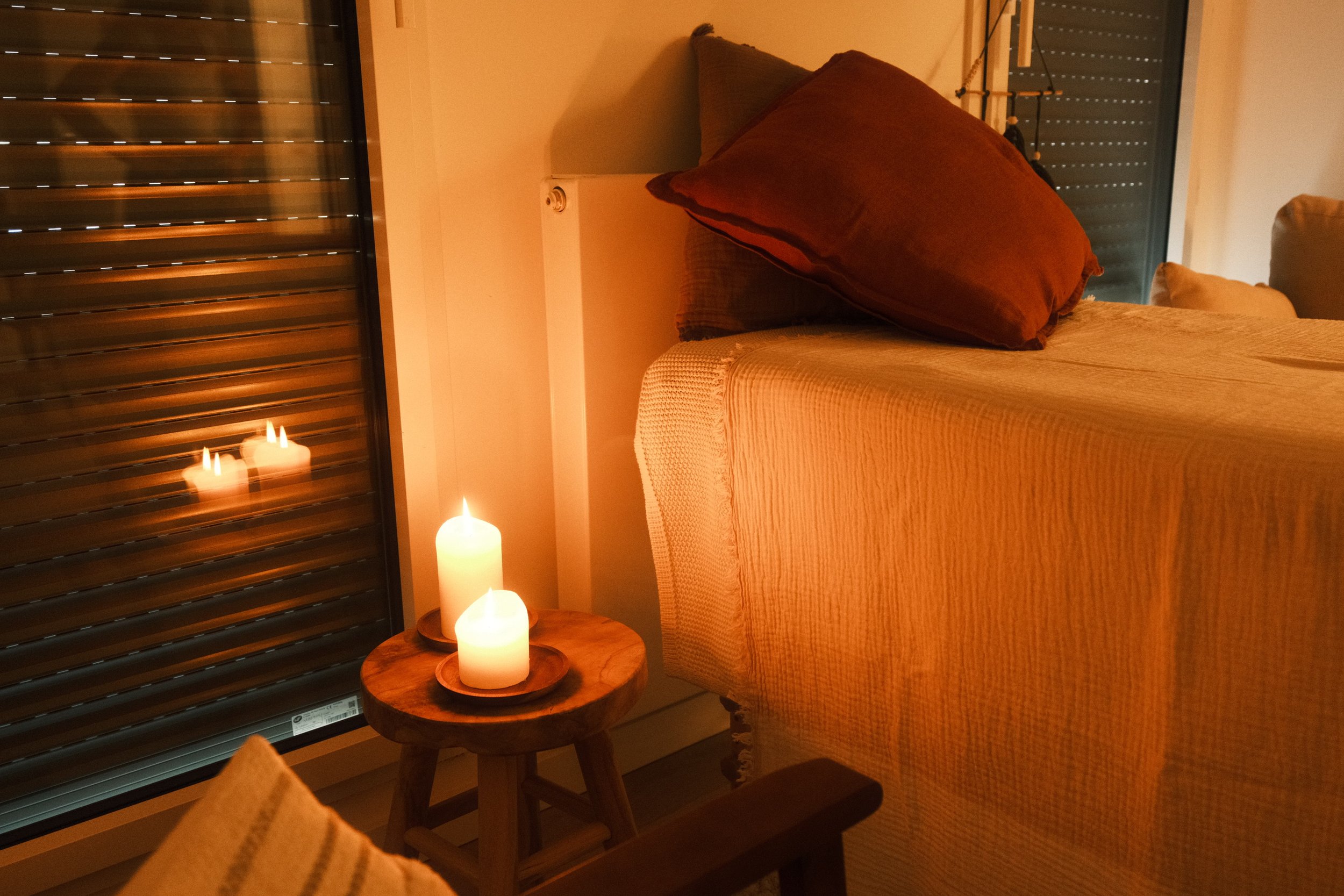 Gros plan sur la table de massage, recouverte de coussins de différentes couleurs, avec des bougies allumées sur une petite table en bois dans une ambiance chaleureuse.