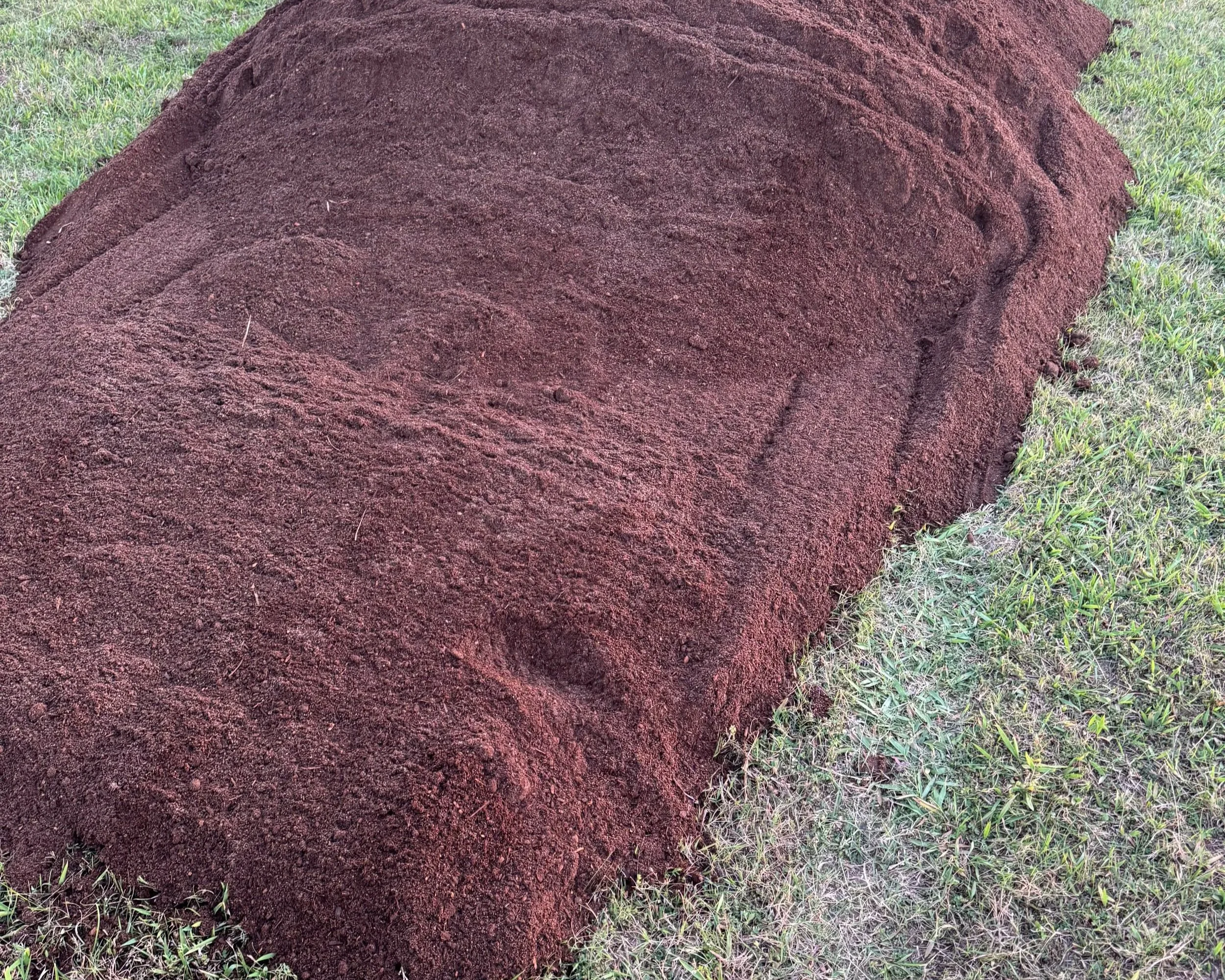A large mound of raised bed compost from Quick Pony Farms in Gainesville Texas on a grassy lawn.