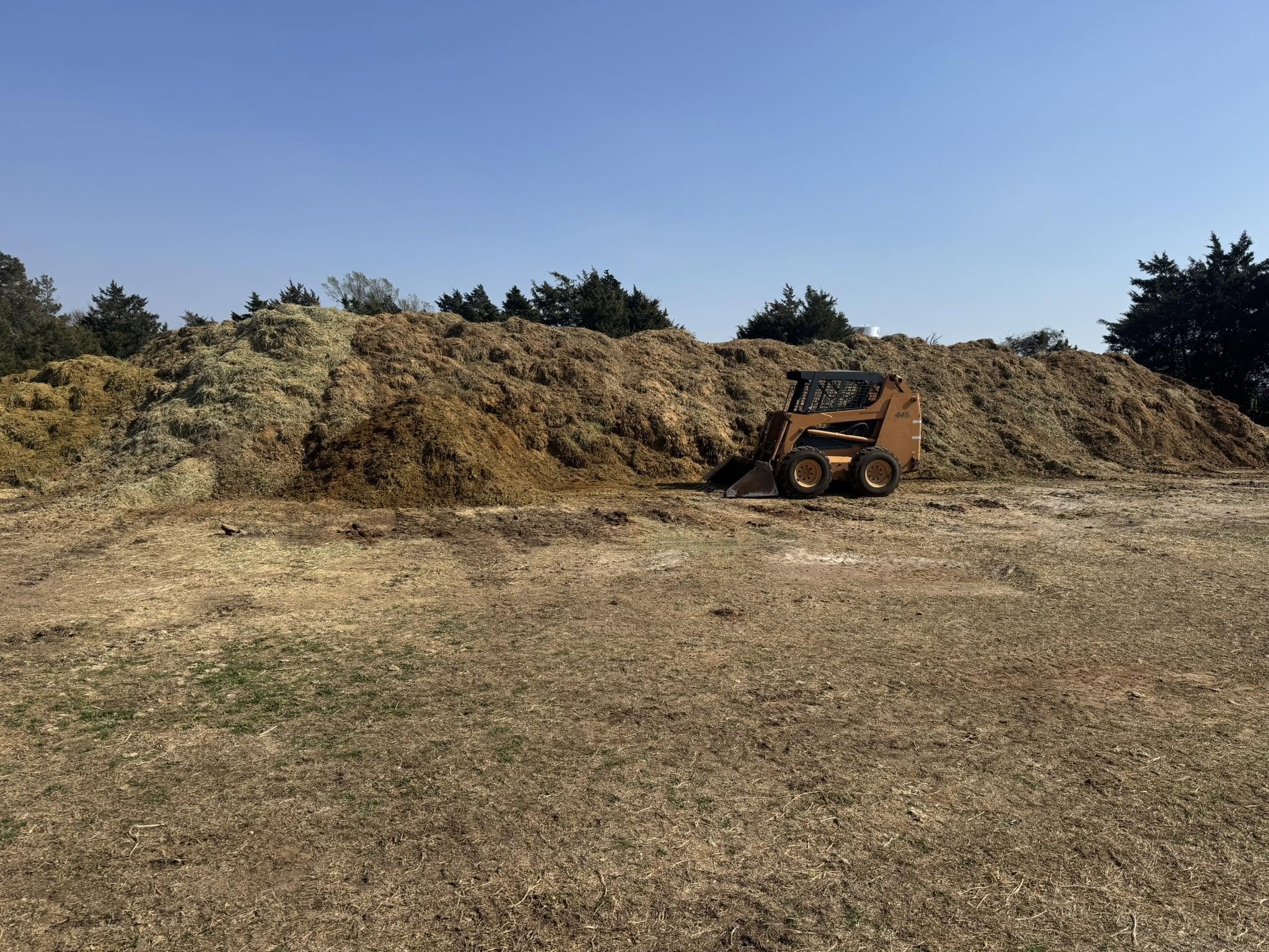 A skid steer loader removing a large pile of horse manure near Gainesville Texas.