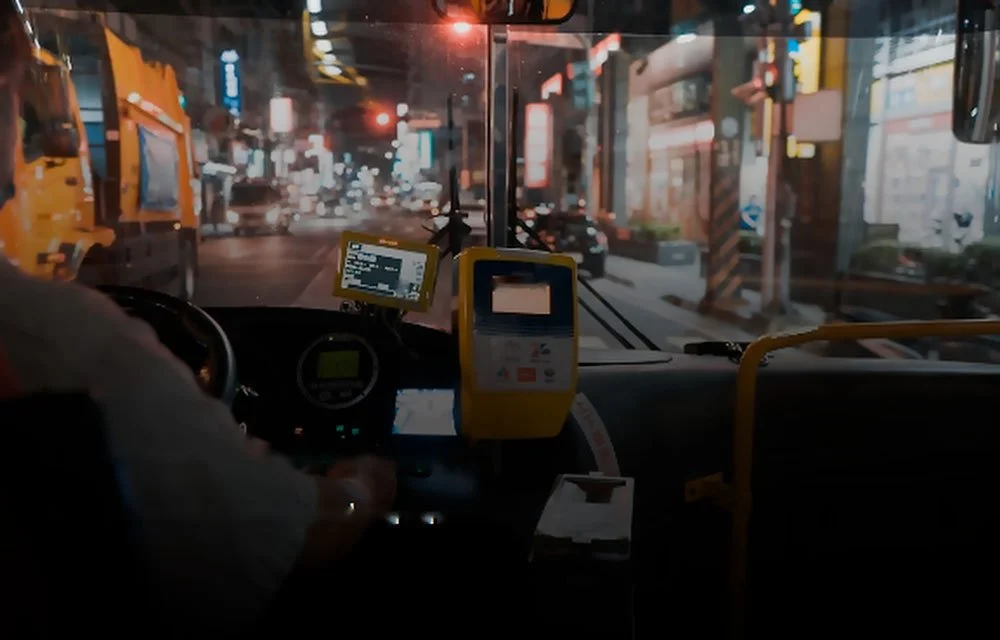 Bus operator seated at the driver workstation during nighttime city service.