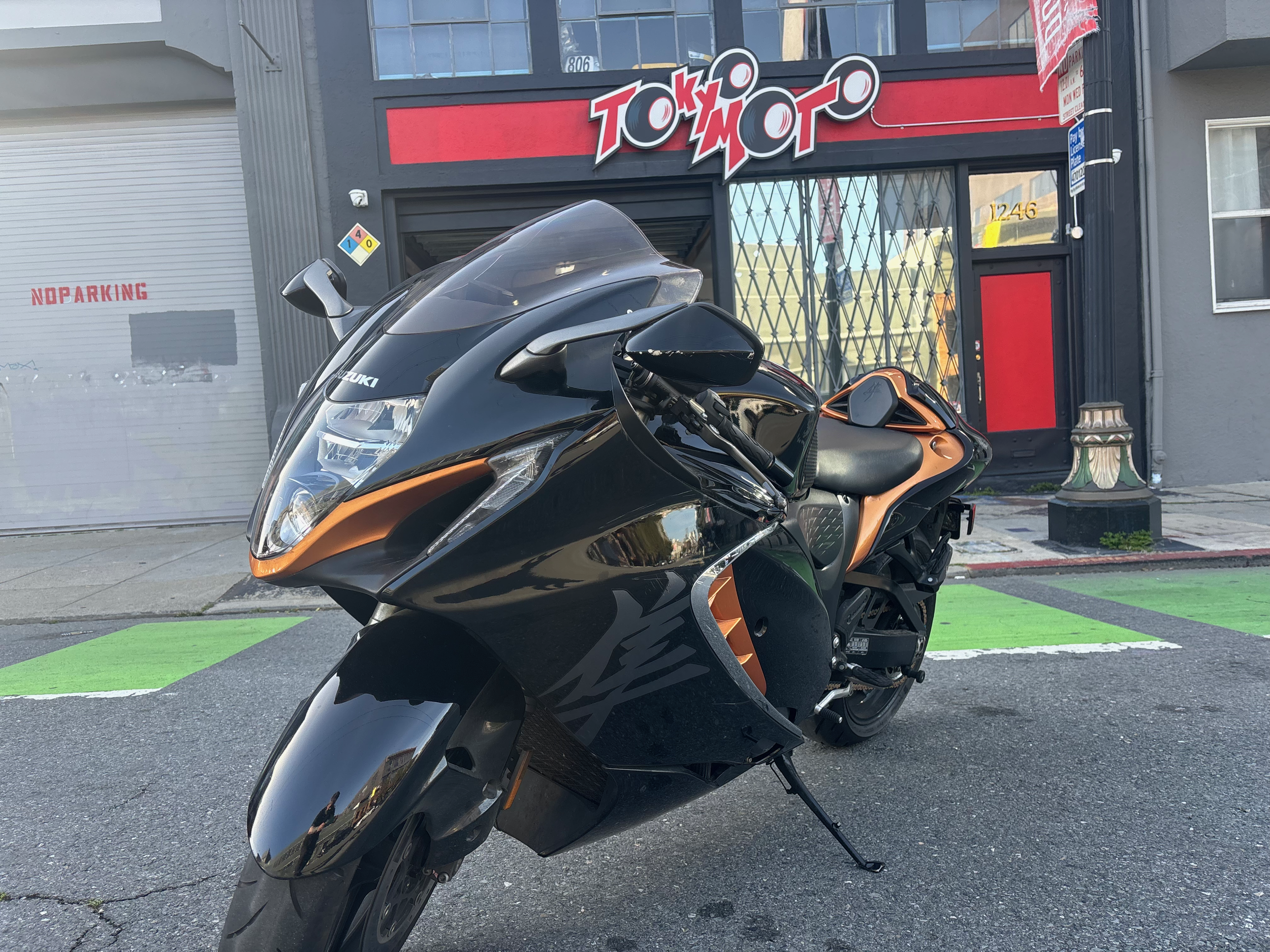 A black and orange motorcycle parked in front of a storefront with a red and black sign that reads "Tokyo Moto."