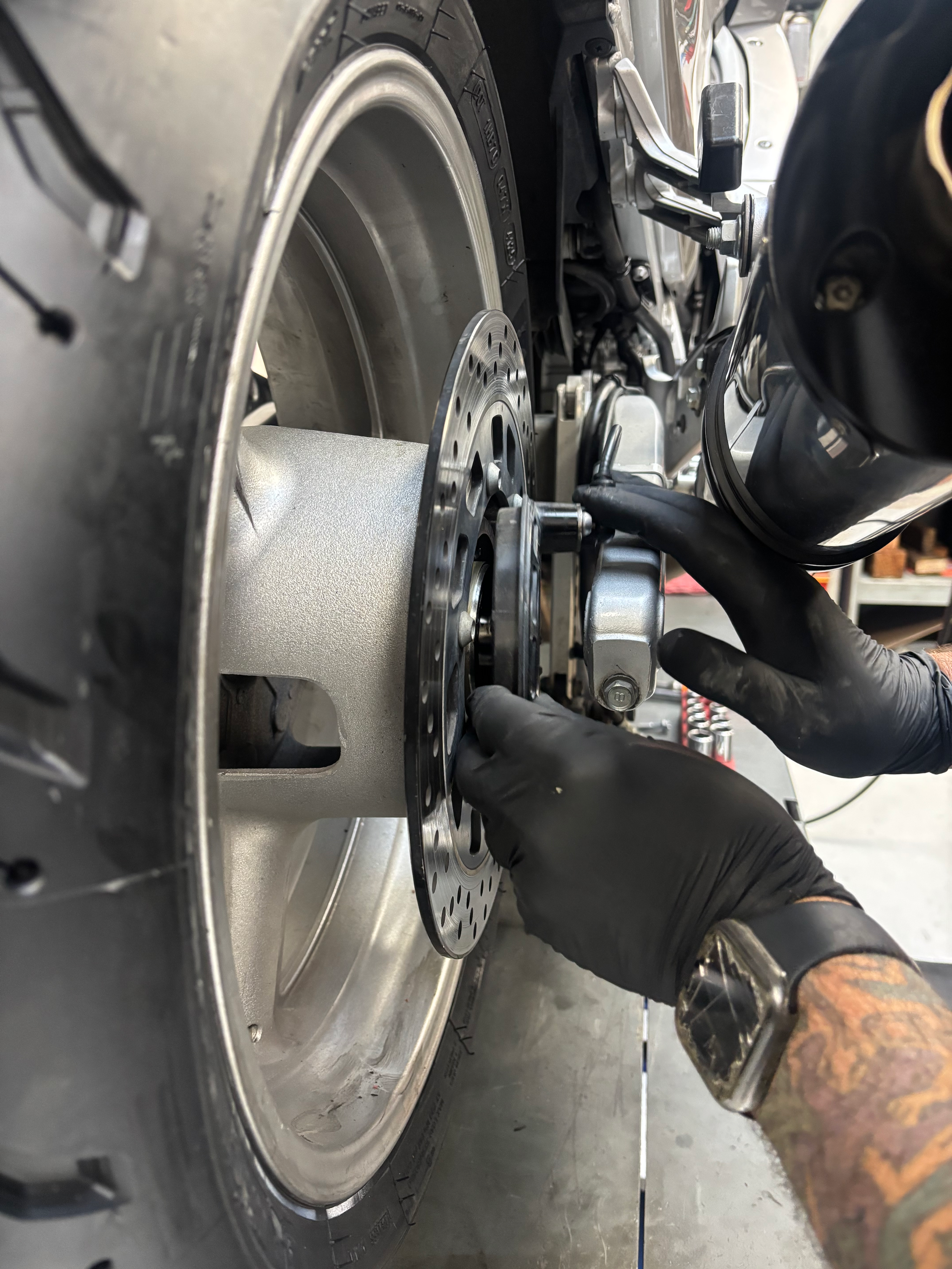 Close-up of a person with tattooed arm using a wrench to work on a motorcycle engine, with focus on the metallic parts and black gloves.