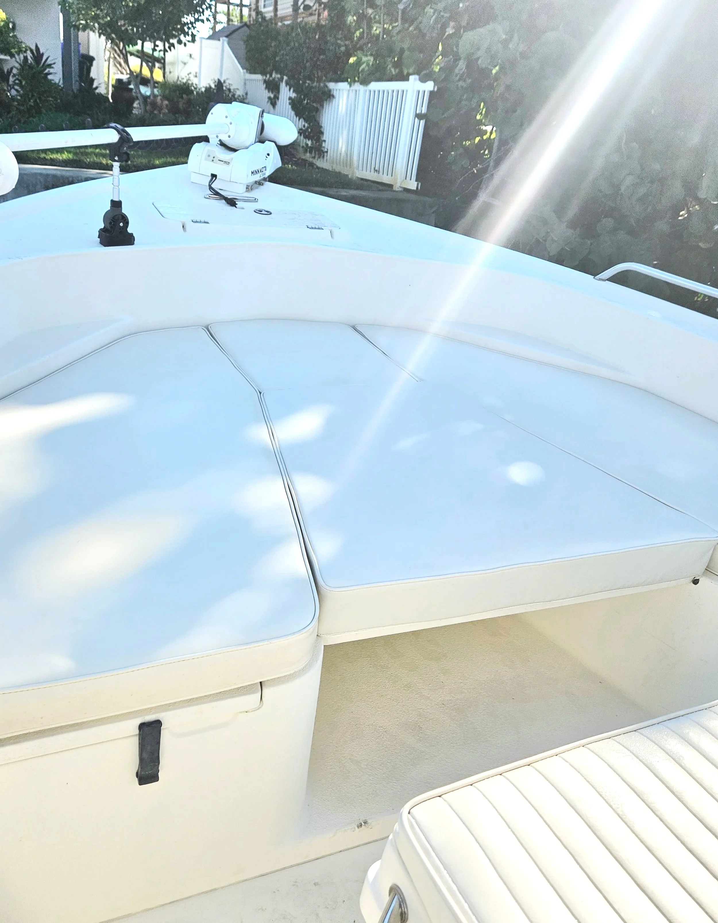 Close-up of a white boat with a radar device mounted on the bow, situated on a porch or deck area with a white fence and bushes in the background, and sunlight shining brightly.