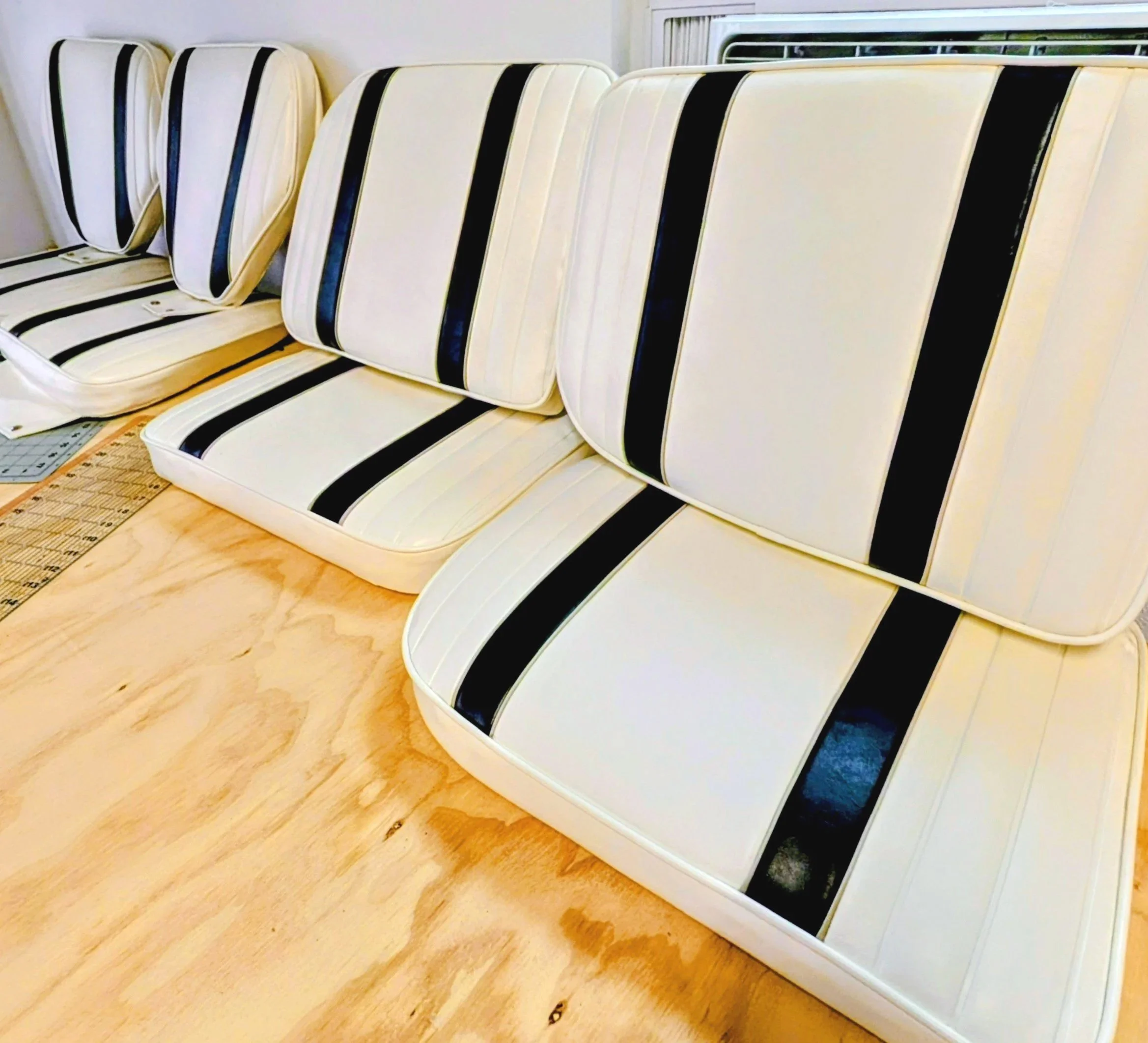 Multiple white mattresses with black and yellow stripes stacked vertically against a wall near a window, on a wooden floor.