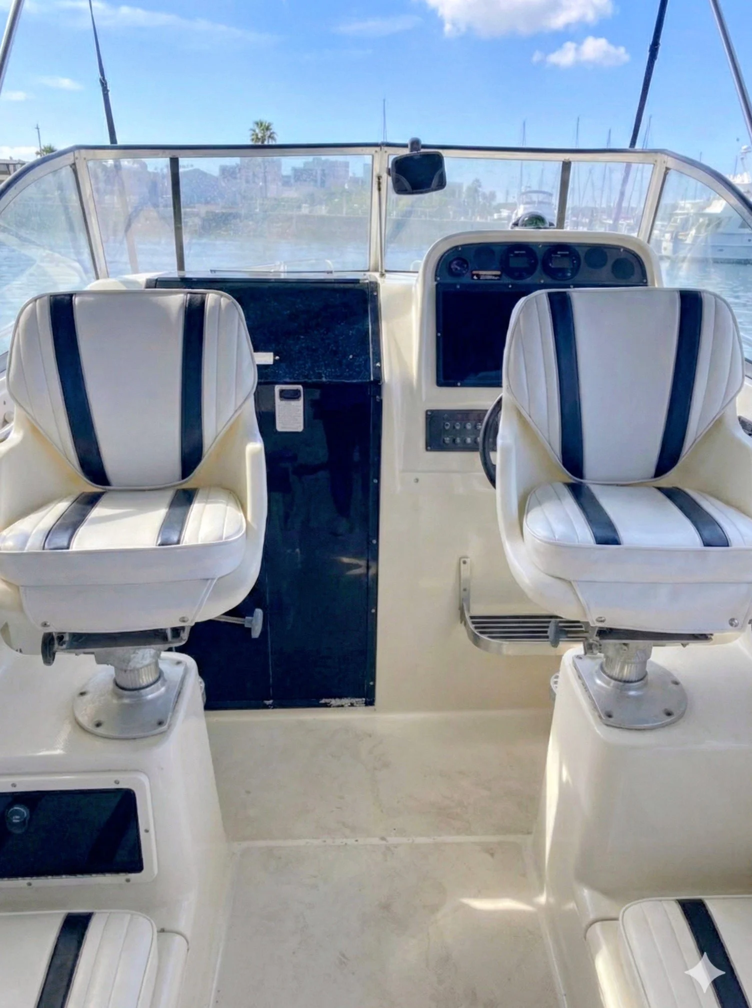 Interior view of a boat with two white cushioned seats with black stripes, a navigation dashboard with GPS and gauges, and a clear windshield with a view of a marina and blue sky outside.