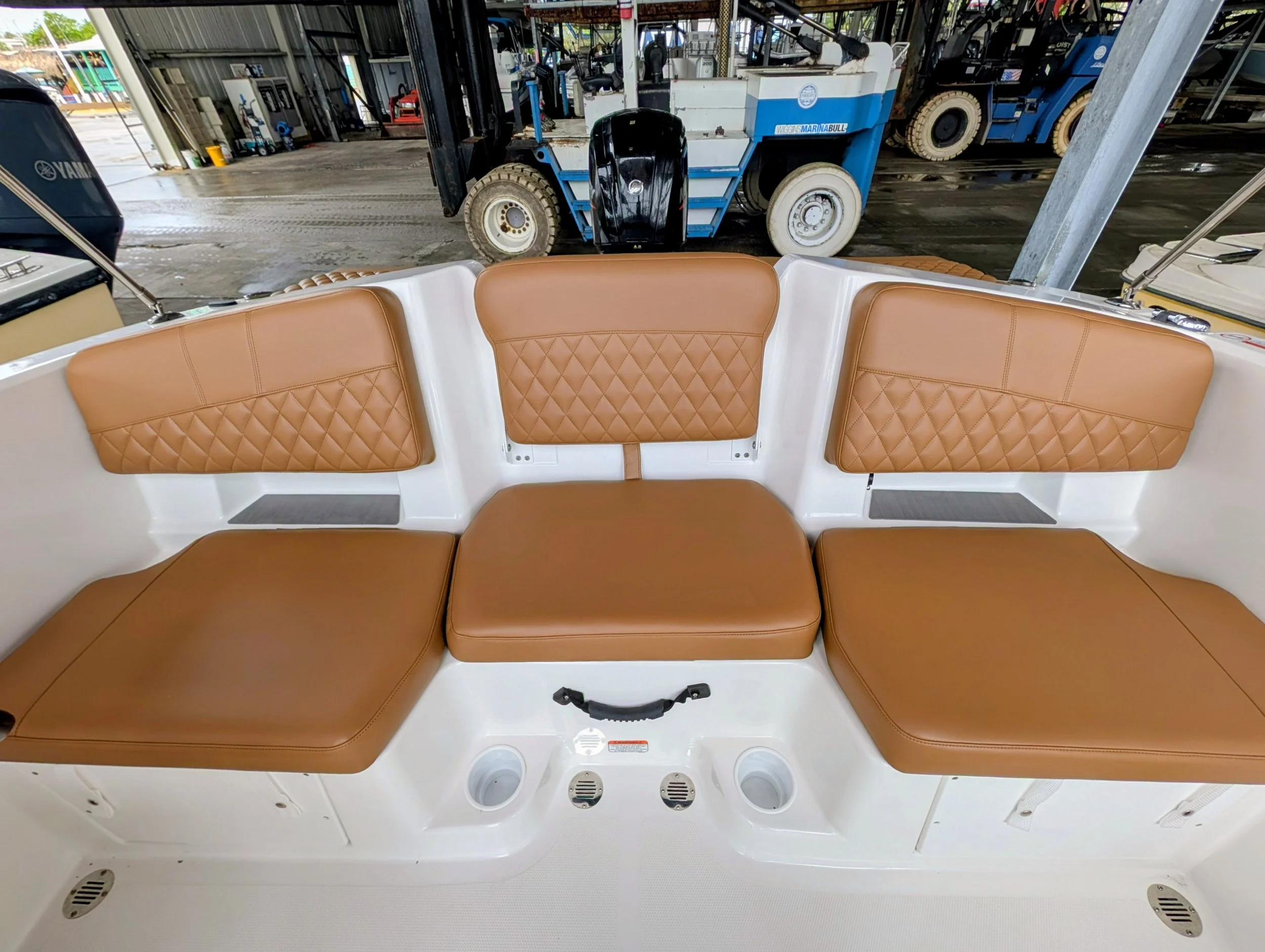 View from inside a boat showing brown cushioned seating and storage compartments, with a dock and equipment outside.