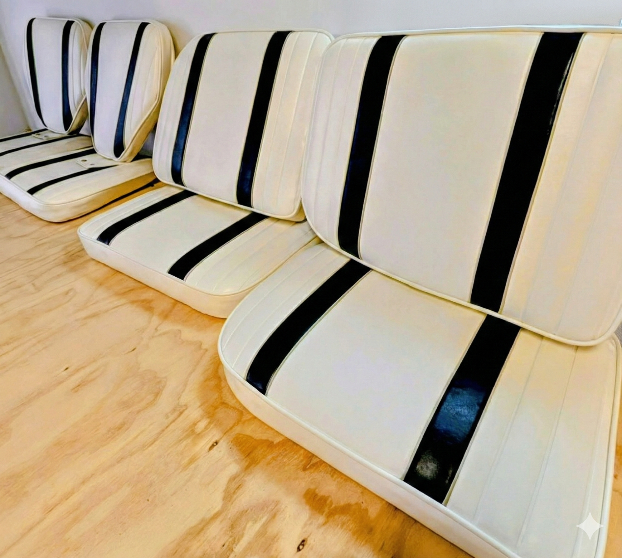 A row of white whale-shaped chairs with black straps, arranged against a plain white wall on a wooden floor. Captains chairs with white quilted marine vinyl