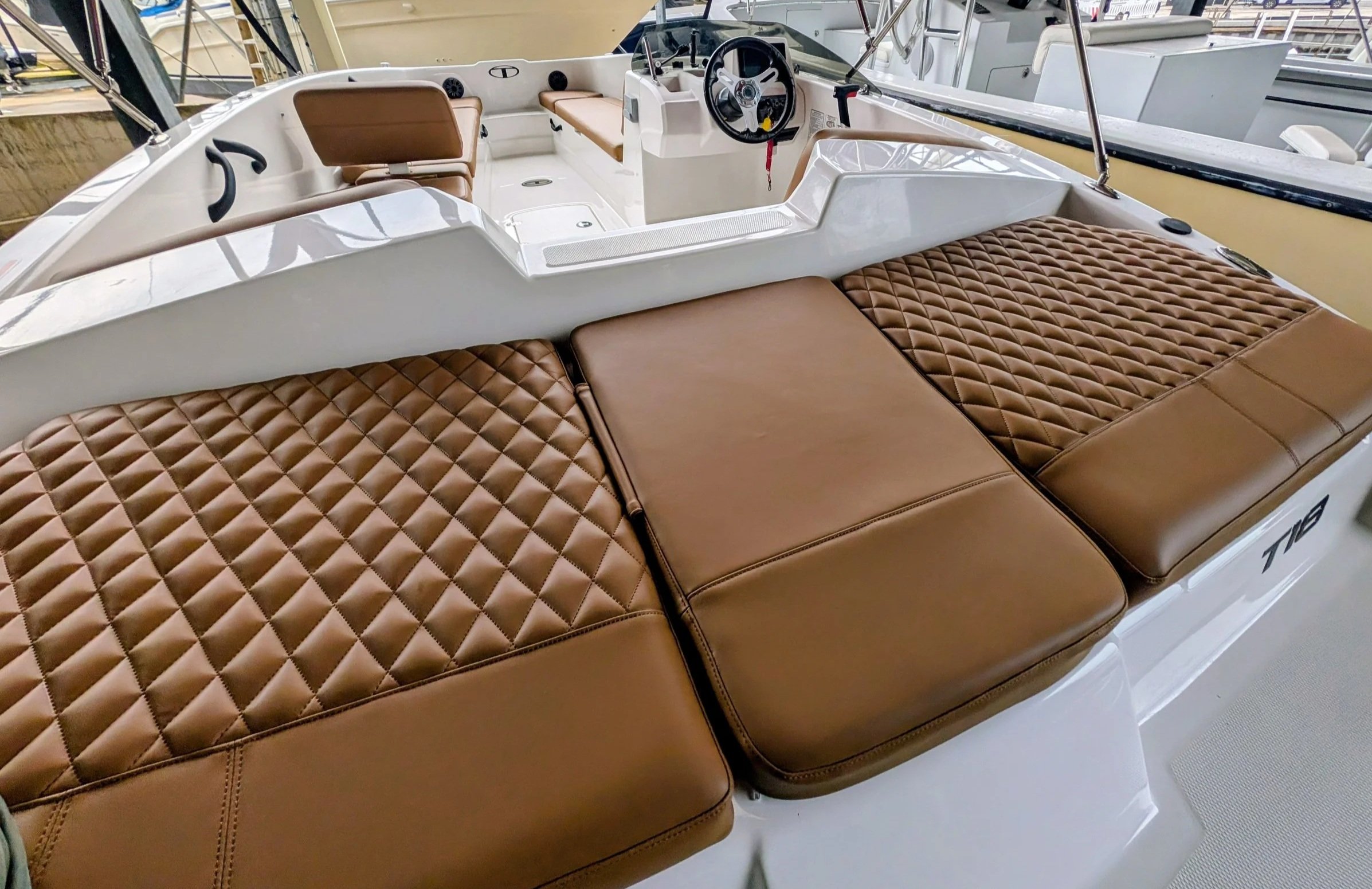 Interior of a boat with tan quilted cushions, tan seats, a steering wheel, and navigation controls, docked at a marina. Diamond quilting and diamond pleats. Quality marine upholstery.