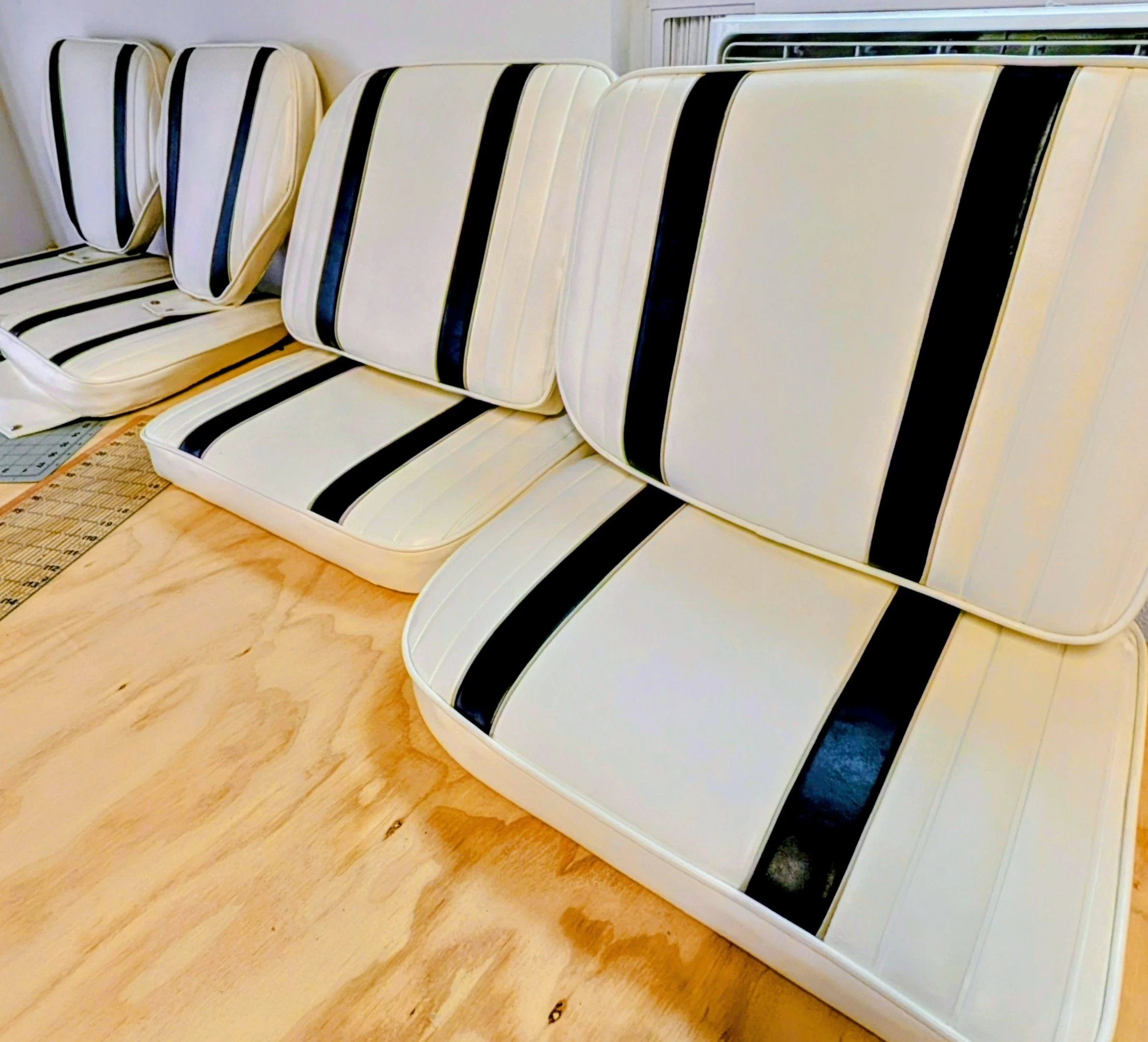 Row of white cushions with black stripes leaning against a wall indoors.