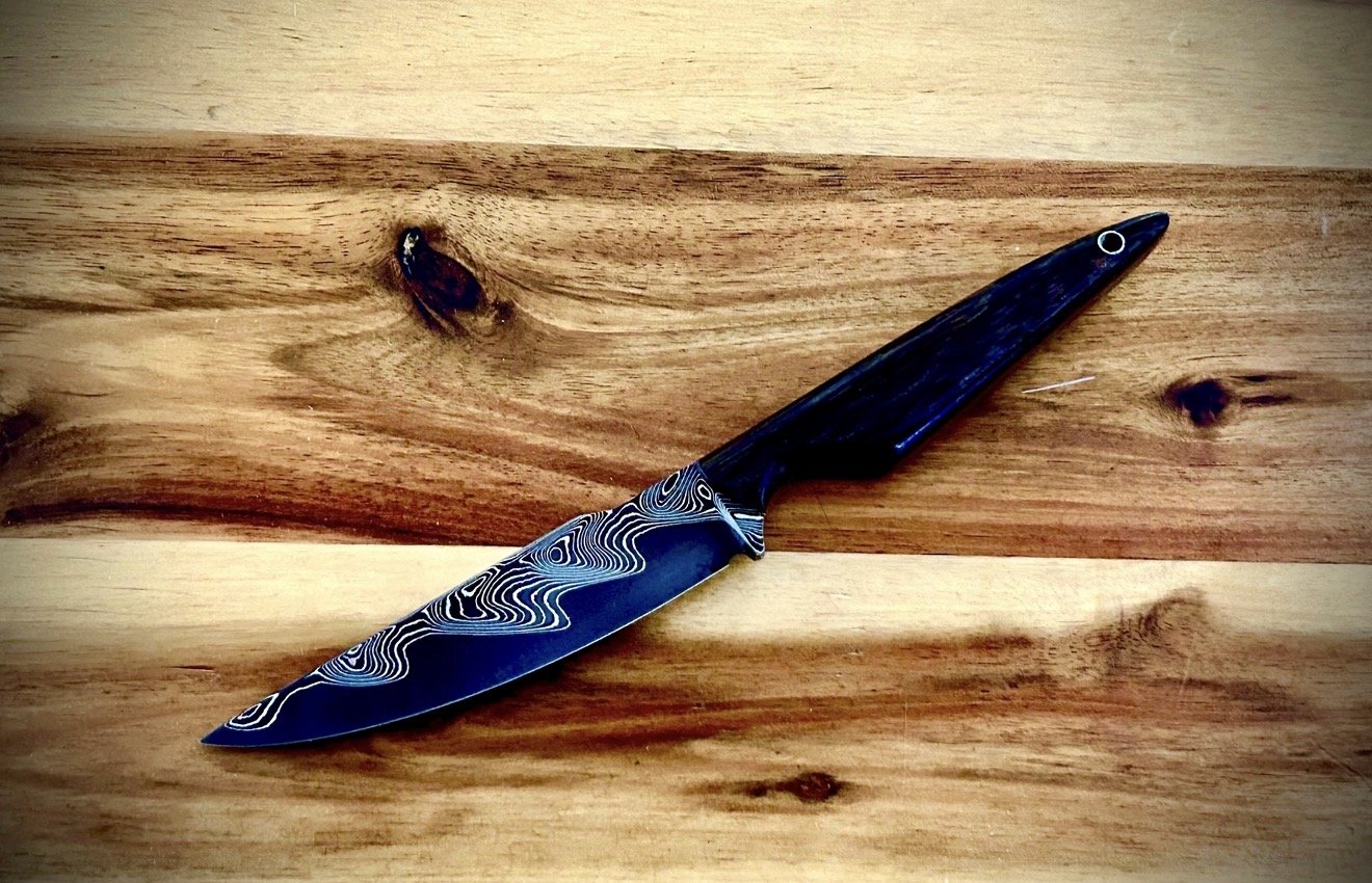 A Damascus steel knife with a black handle on a wooden surface.