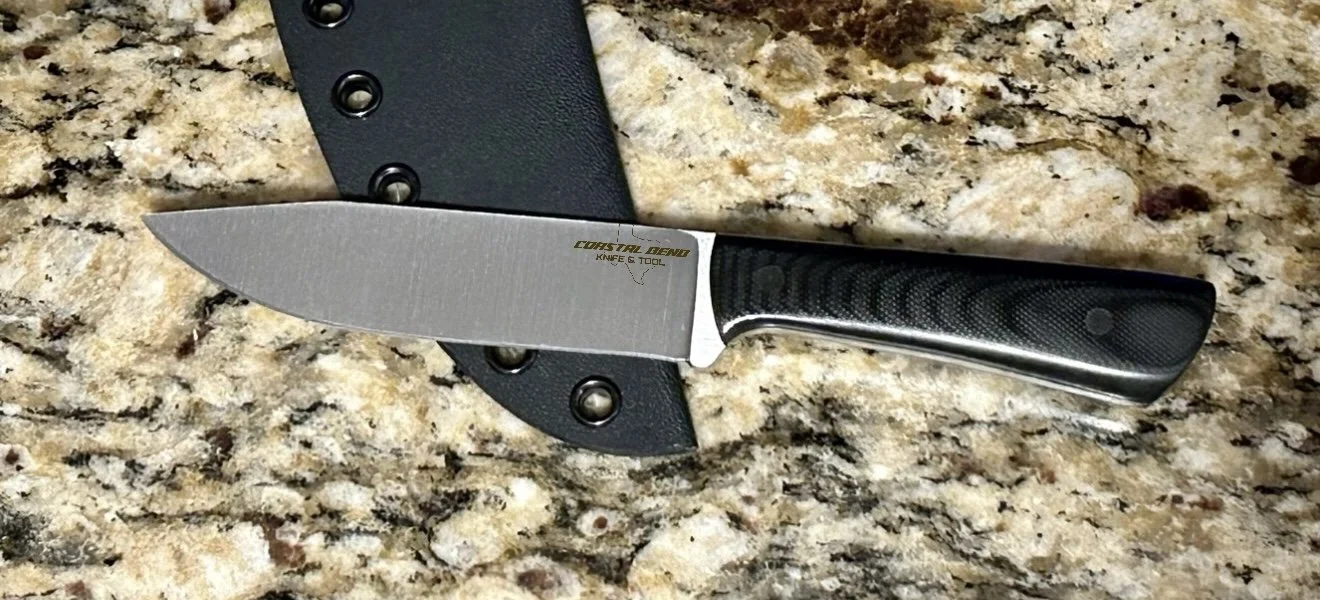 A kitchen countertop with a fixed-blade knife with a black handle and a sharp, pointed blade, resting on a black sheath.