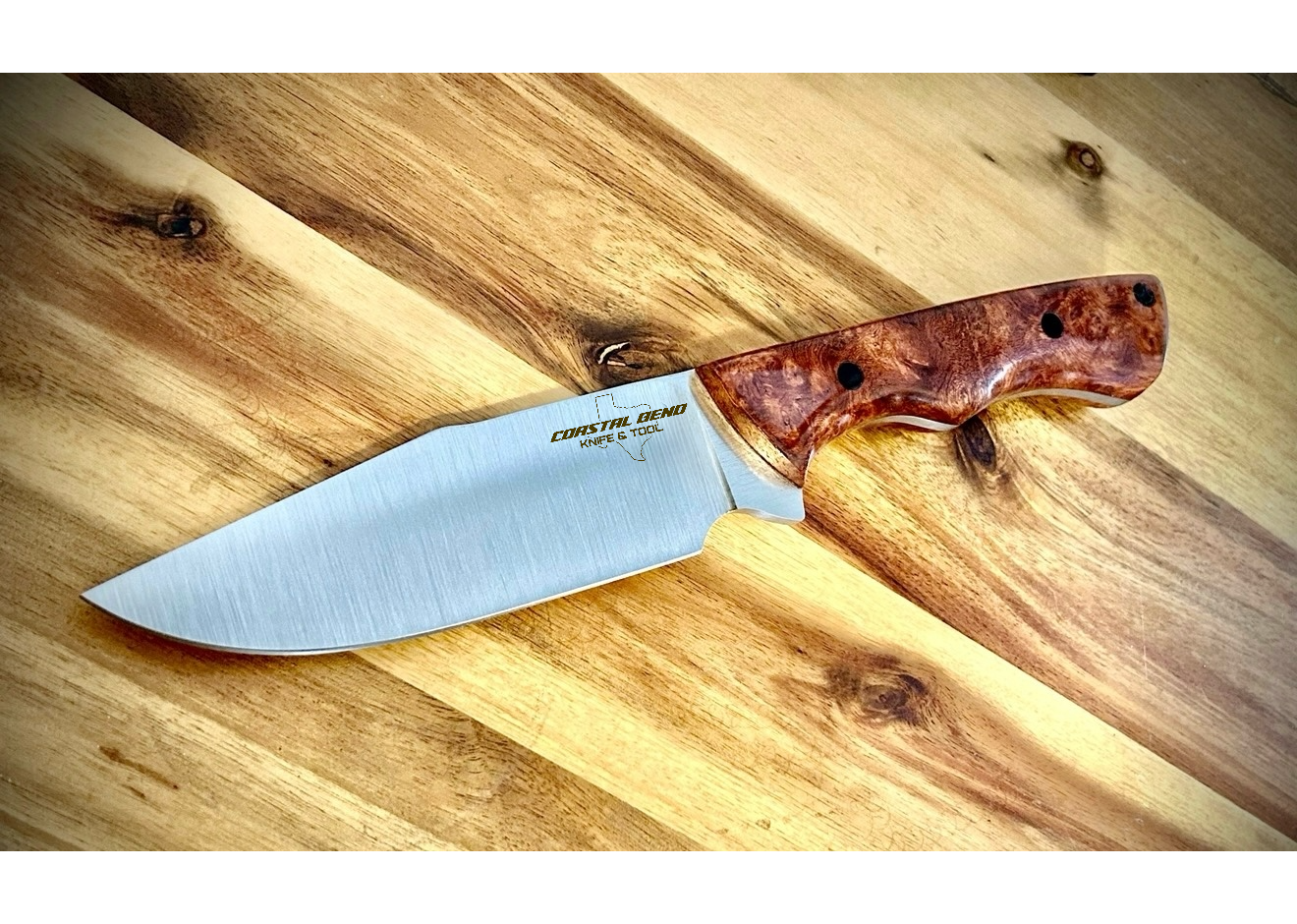 A hunting knife with a wooden handle and a stainless steel blade resting on a wooden surface.