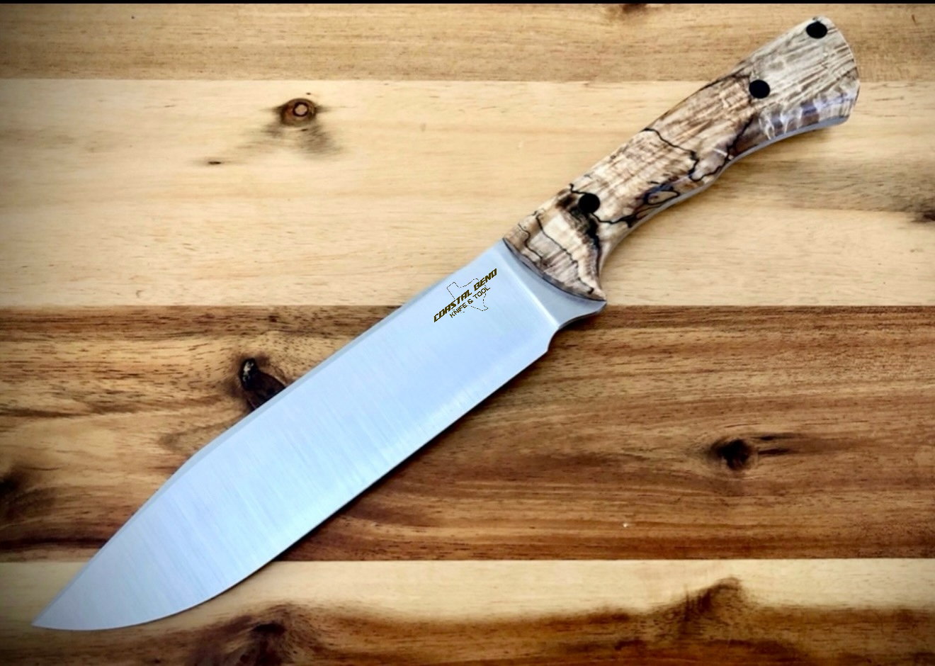 A fixed-blade kitchen knife with a light-colored, textured wooden handle resting on a wooden surface.