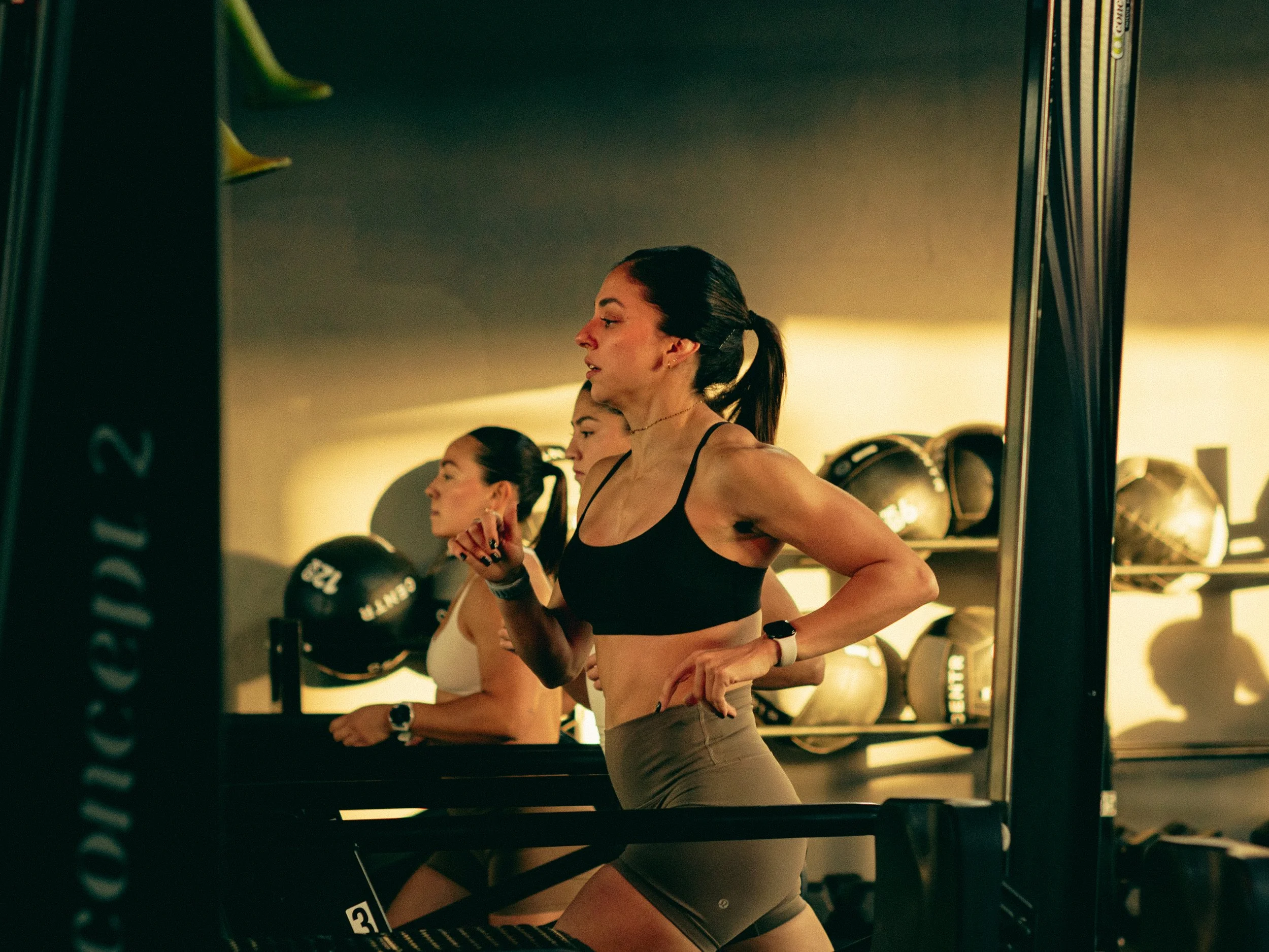 Women working out with dumbbells in a gym, seen in a mirror.