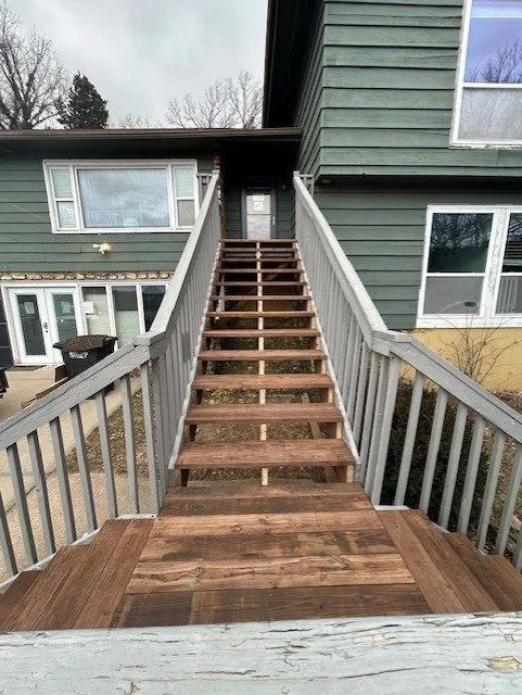 A wooden staircase leading up to a house door, with a small landing at the top, in a residential area.