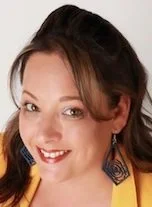 Close-up of a smiling woman with brown hair, wearing yellow clothing and dark earrings
