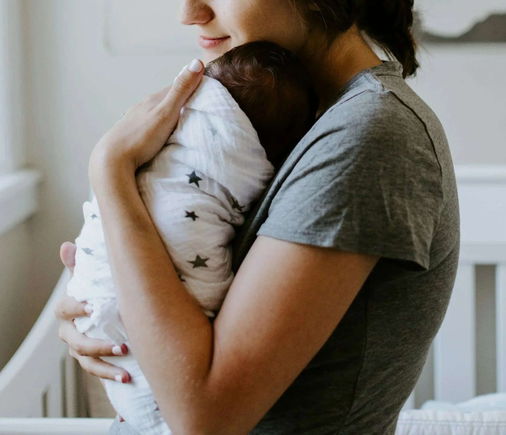 A woman is holding a newborn baby close, gently pressing her face on the baby's head in a caring embrace.