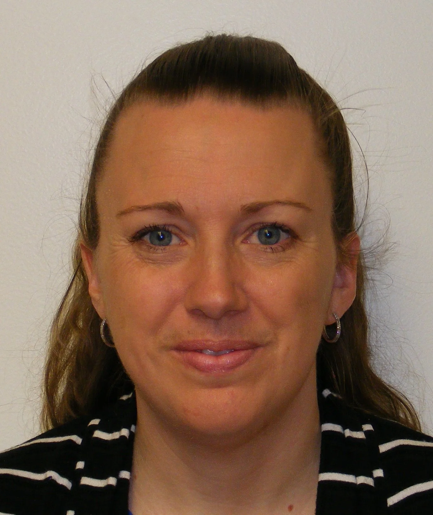 Close-up of a woman with blue eyes, brown hair, earrings, wearing a black and white striped shirt, smiling slightly, against a plain white background.