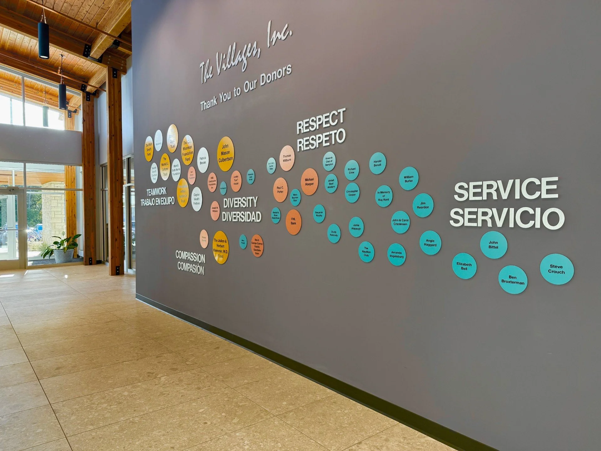 Interior of a building with a wall display honoring donors, featuring words like 'Respect', 'Diversity', 'Compassion', and names on colored circles.