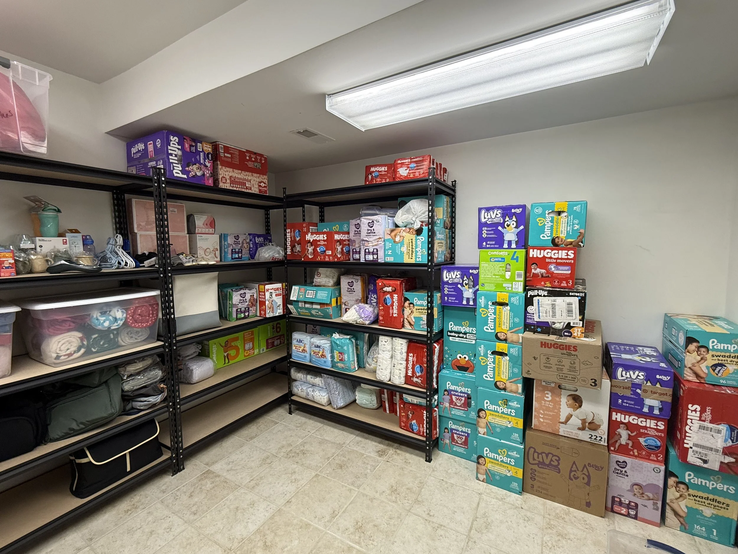 Store room with metal shelves filled with boxes and packages of diapers, baby wipes, and baby care products.
