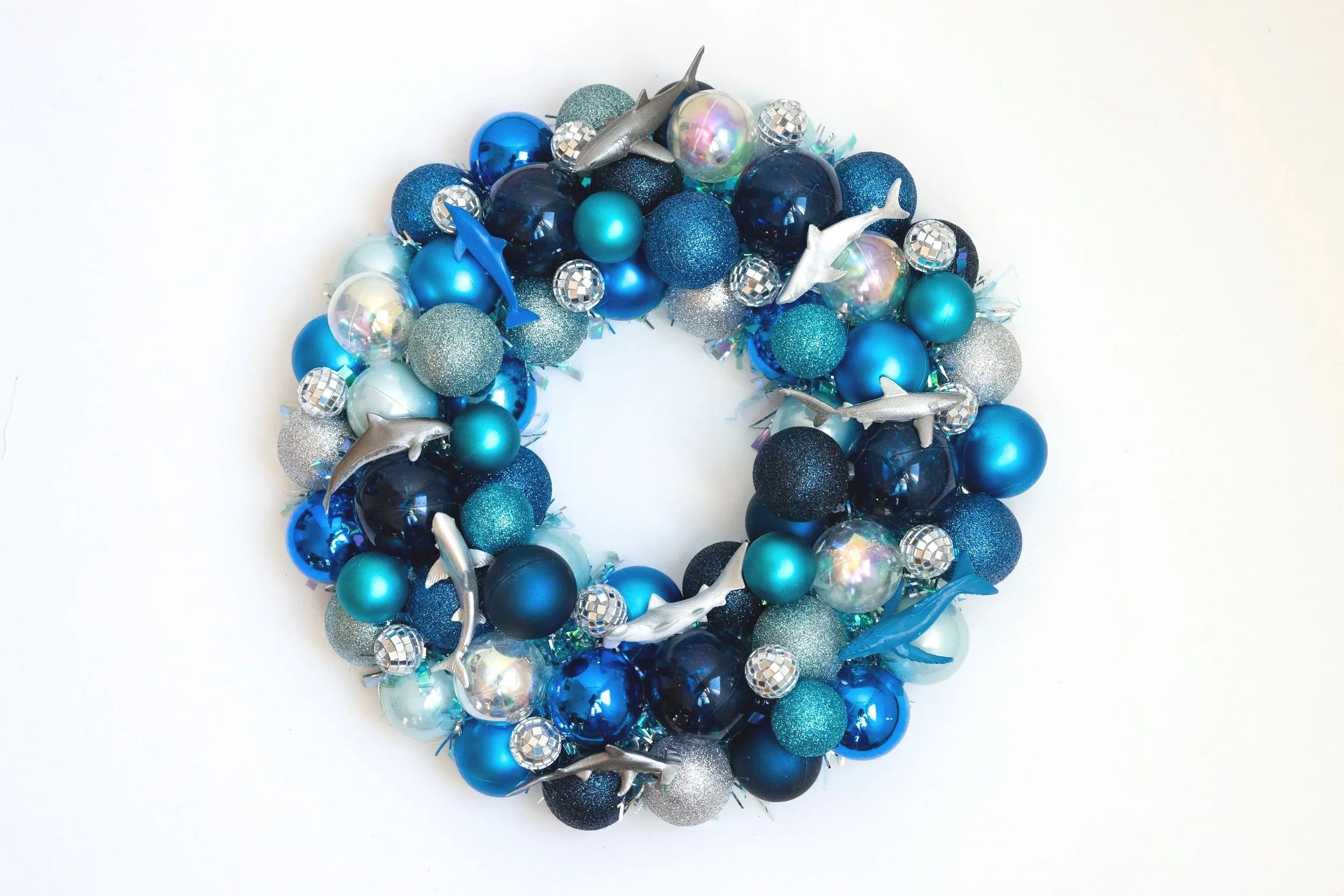 A circular decorative wreath made of shiny blue, silver, black, and iridescent ornaments, including dolphins, whales, sharks and reflective Disco balls.