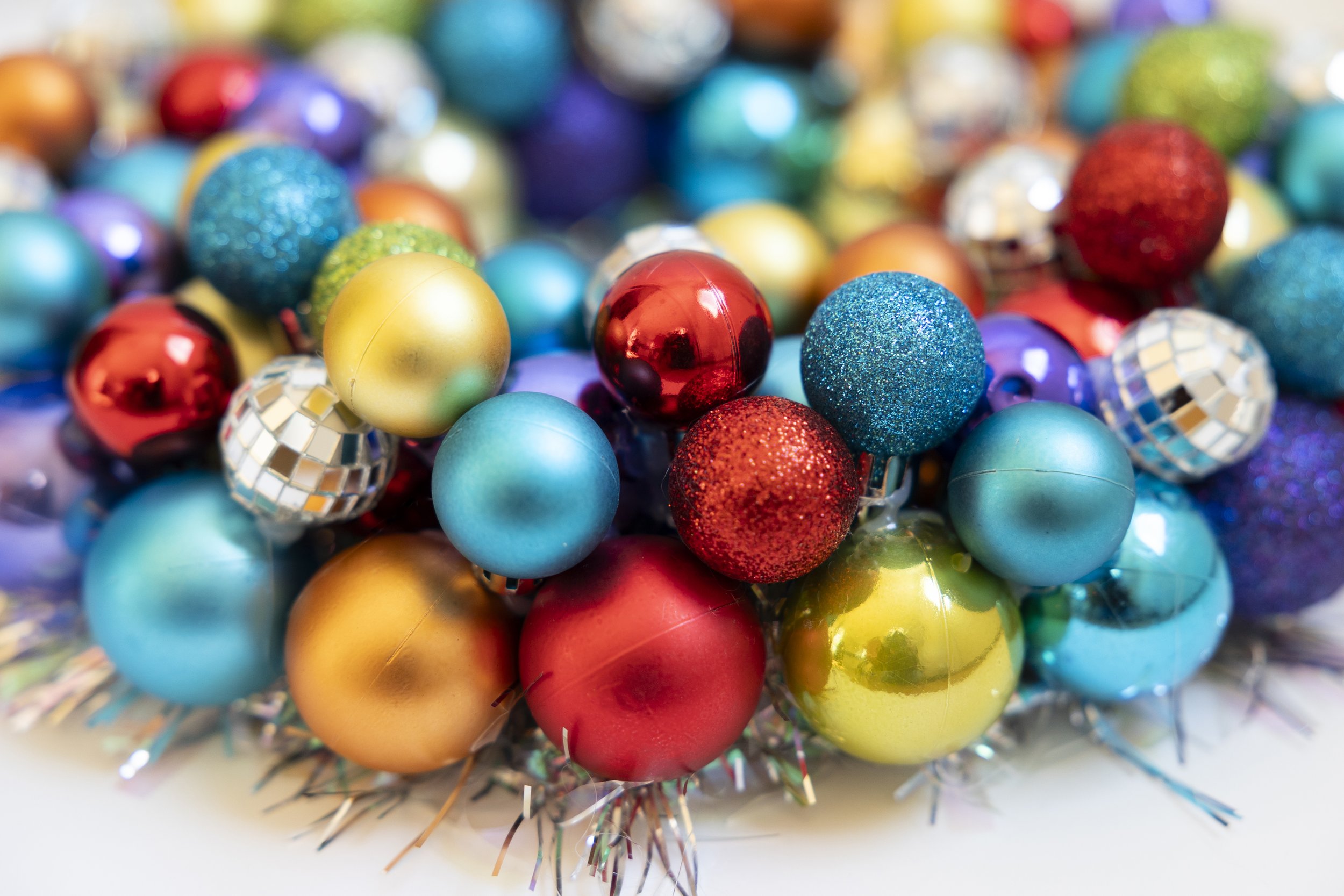 A colorful assortment of Christmas ornaments on a wreath including red, gold, blue, purple, and glittery disco ball spheres, arranged in a decorative display.