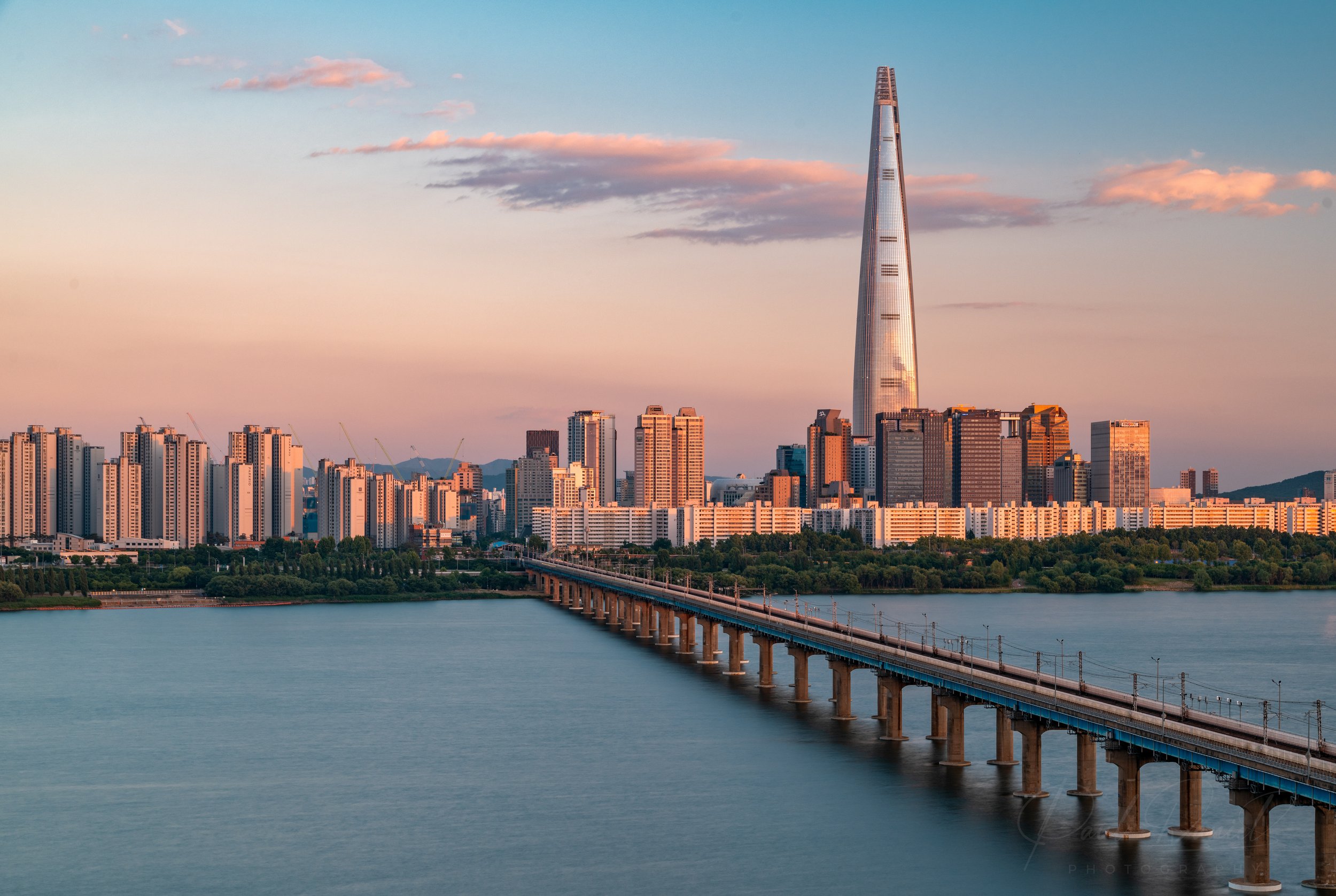 Sunset panoramic landscape of the Han River and Jamsil Railway Bridge leading toward Lotte World Tower and the Jamsil skyline in Seoul, South Korea. 