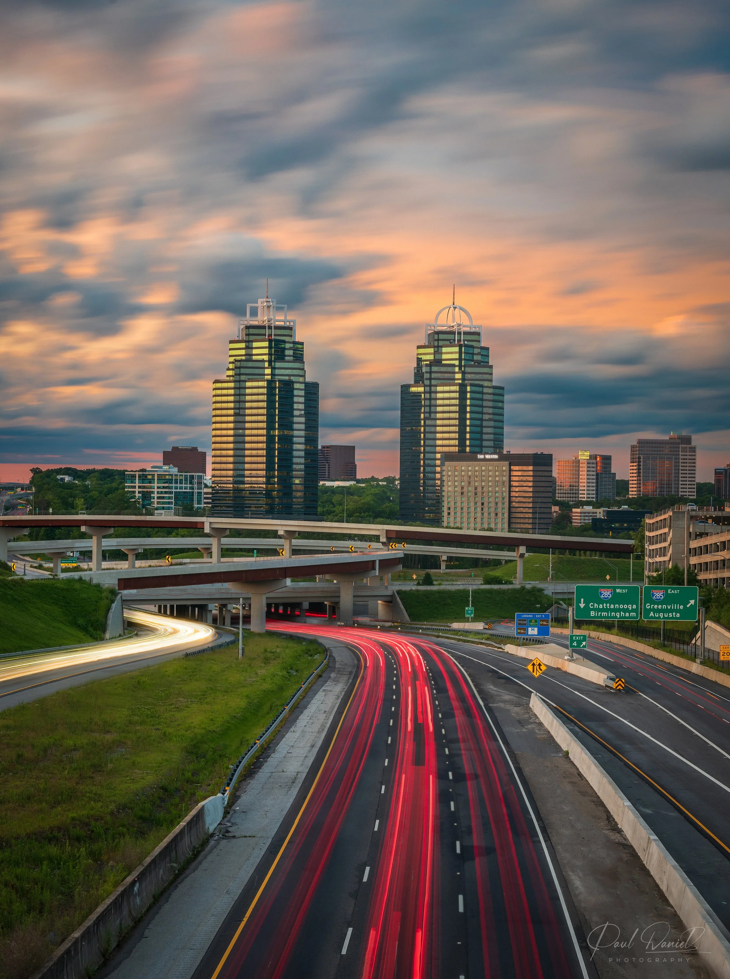 King and Queen towers at Concourse Center at sunset with long-exposure highway traffic light trails in Sandy Springs, GA.