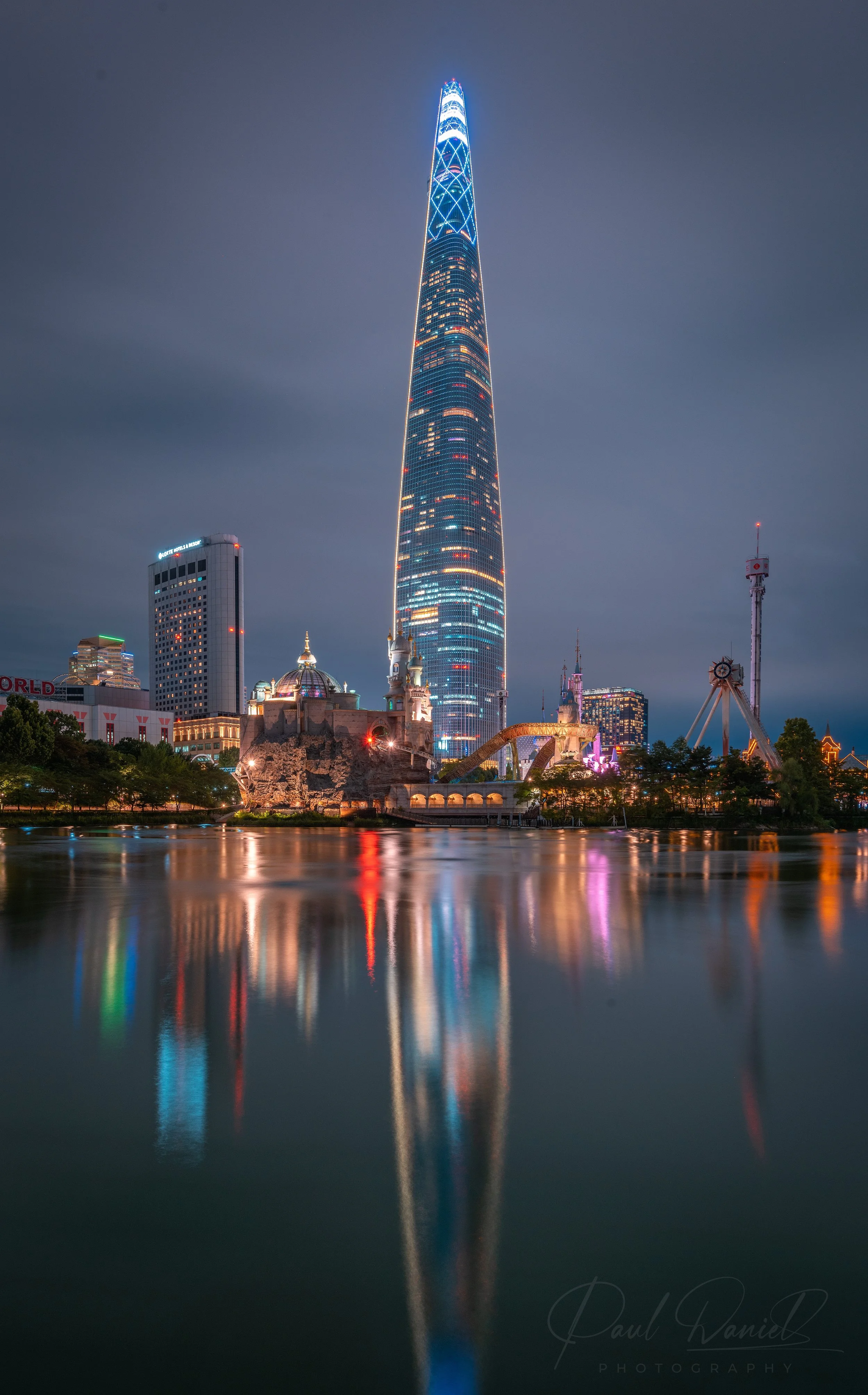 Vertical night photo of the illuminated Lotte World Tower reflected in Seokchon Lake in the Jamsil district of Seoul, South Korea