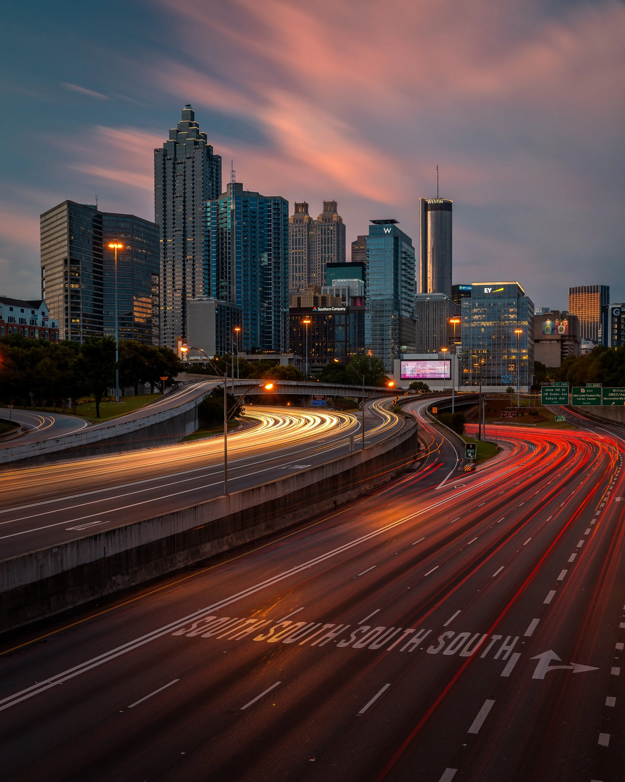 Downtown Atlanta skyline at sunrise from North Avenue, featuring 191 Peachtree Street, Westin Peachtree Plaza, Truist Plaza, and sweeping highway light trails on the Connector